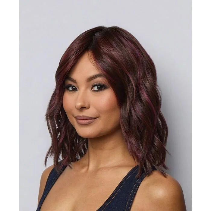 Woman with shoulder-length wavy hair in shades of burgundy and purple, wearing a dark sleeveless top, smiling slightly, against a plain light background.