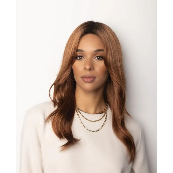 A woman with long, wavy, reddish-brown hair wearing a white top and layered gold necklaces