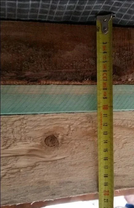 Une règle de mesure en métal jaune posée verticalement sur du bois. La règle indique une hauteur d'environ 16,5 centimètres.