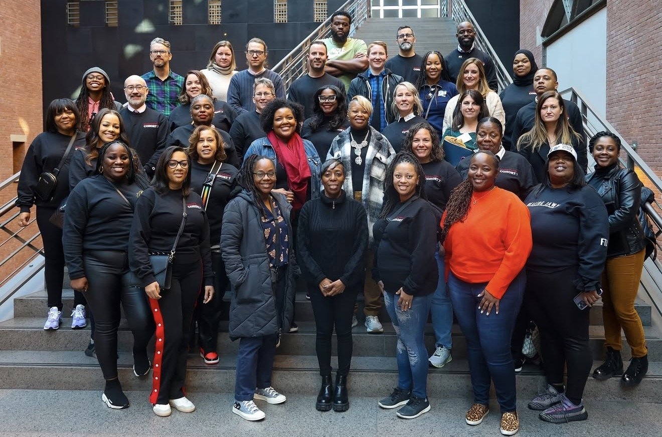 A large group of diverse people gathered on a staircase inside a modern building, posing for a group photo.