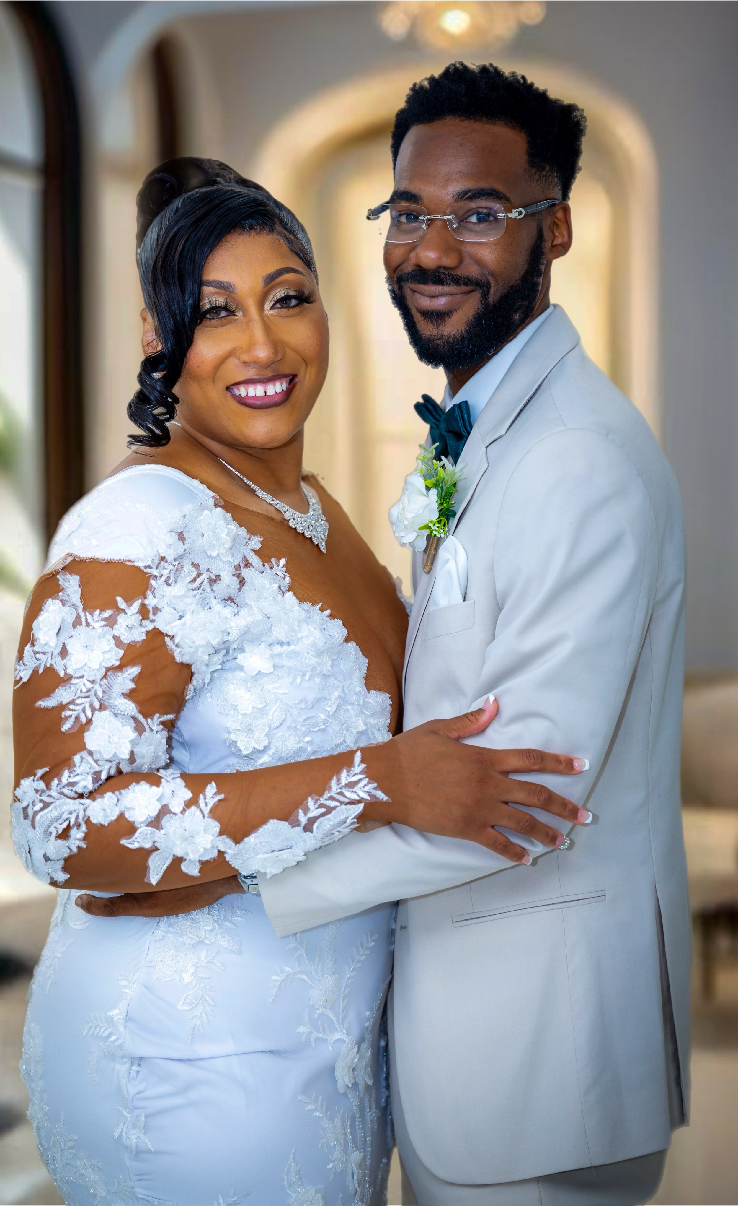 A bride and groom in wedding attire, smiling and holding each other indoors with a bright, elegant background.
