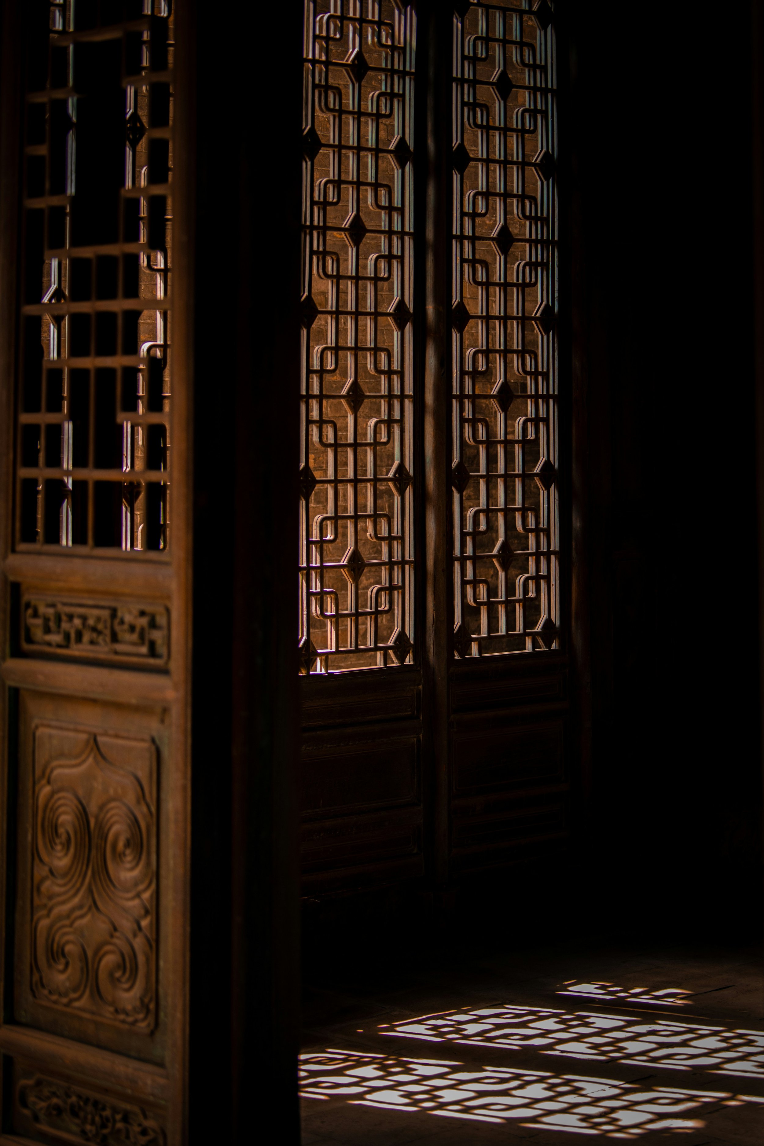 Intricate wooden lattice doors with sunlight casting geometric shadows on the floor.