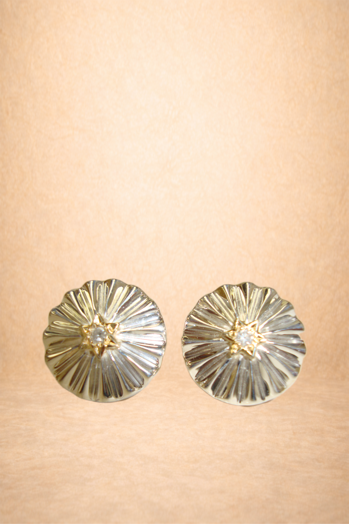 Pair of gold and silver stud earrings with a star-shaped design in the center, displayed on a peach-colored surface.