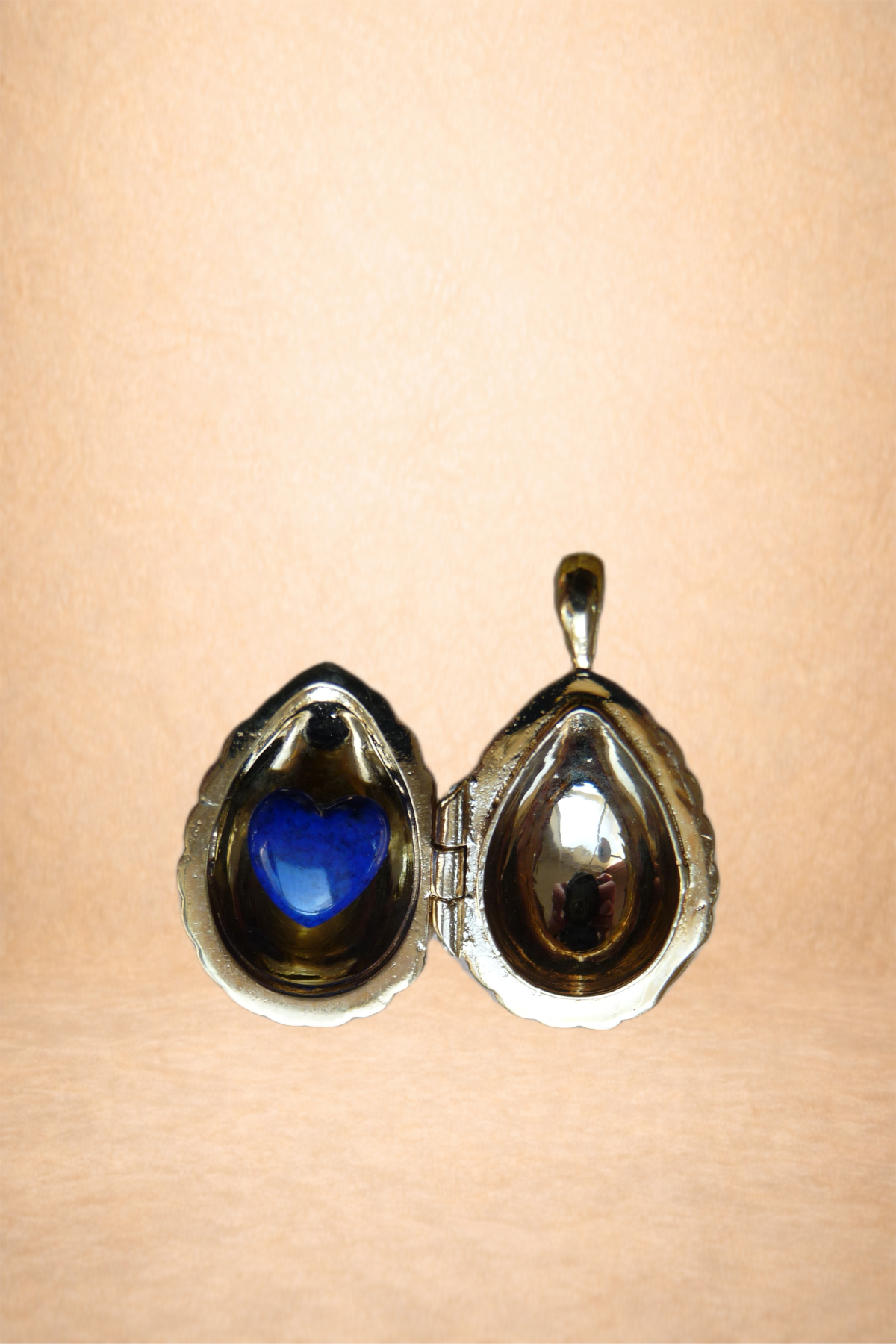 Open jewelry box shaped like an oyster shell with a blue heart-shaped gem inside and reflections on the interior surfaces.