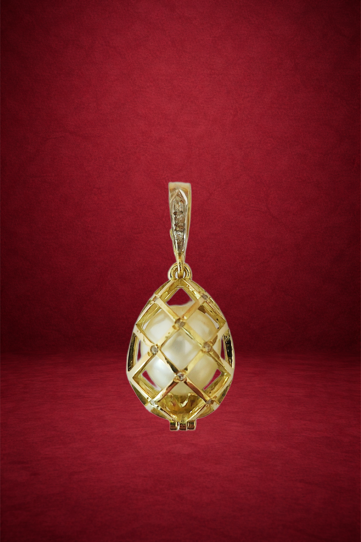 Gold pendant featuring a lattice design with a large pearl inside, hanging against a red background.