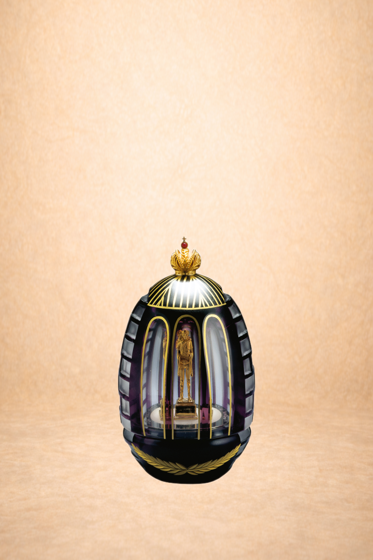 A decorative egg-shaped object with black and purple vertical stripes, gold detailing, and a small gold statue inside, topped with a gold crown and a red jewel.