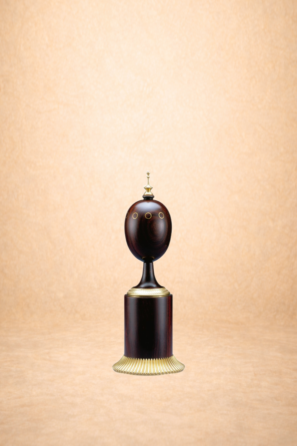 An ornate, dark wooden, egg-shaped ornament with gold accents, mounted on a black and gold stand, against a plain beige background.