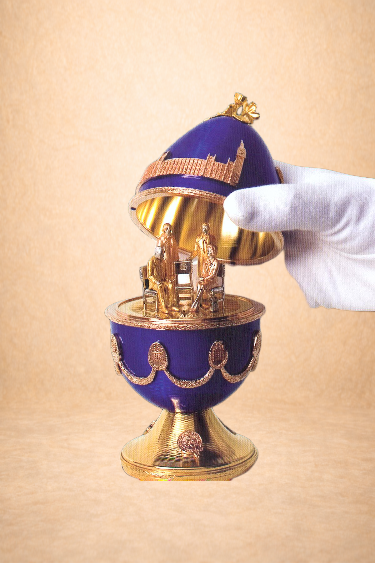 A decorative souvenir egg with a royal blue and gold design, featuring a miniature sculpture of three people inside and a gold and purple topped lid with landmarks and chains decorated on it.