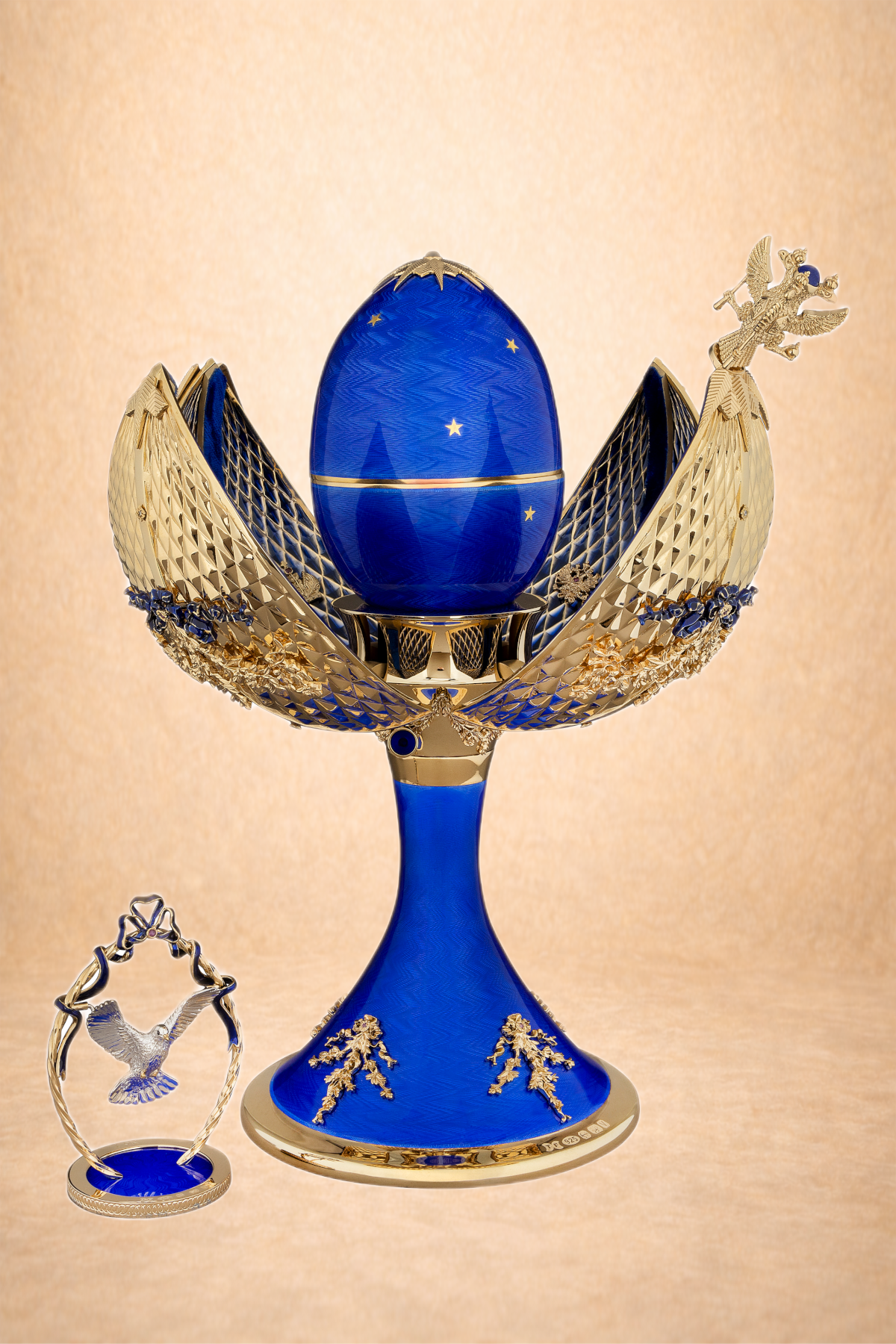 A decorative blue egg encased in a golden and blue lotus flower-shaped stand with intricate details, accompanied by a small gold and blue hummingbird figurine.