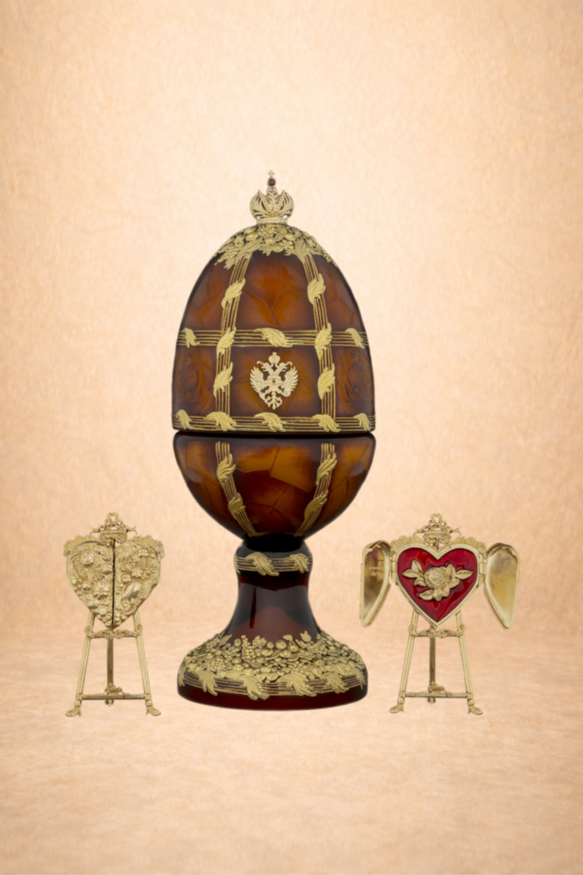 Decorative religious artifacts including a large brown and gold egg with intricate gold detailing and two smaller gold and red heart-shaped items on stands, displayed against a beige background.