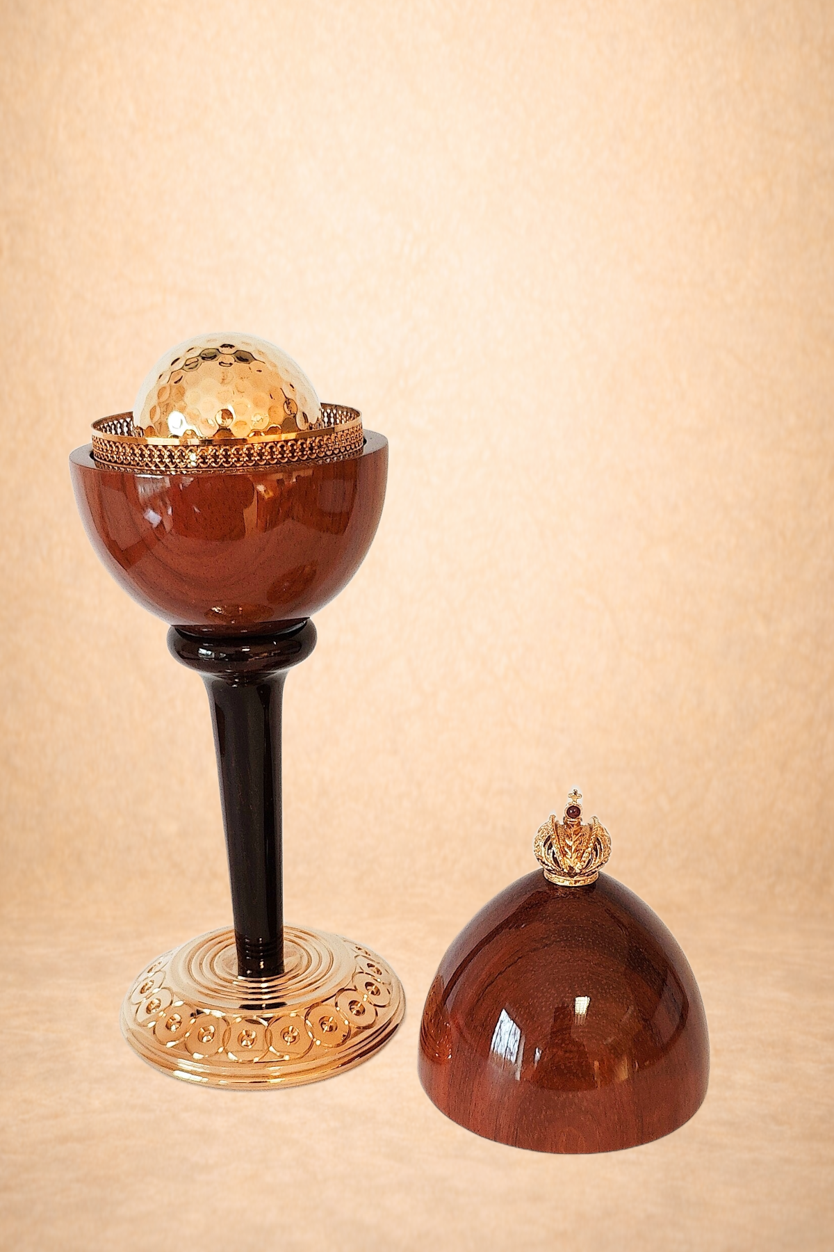 A decorative glass display with a gold sphere on a stand, gold crown, and a wooden dome-shaped object against a beige background.