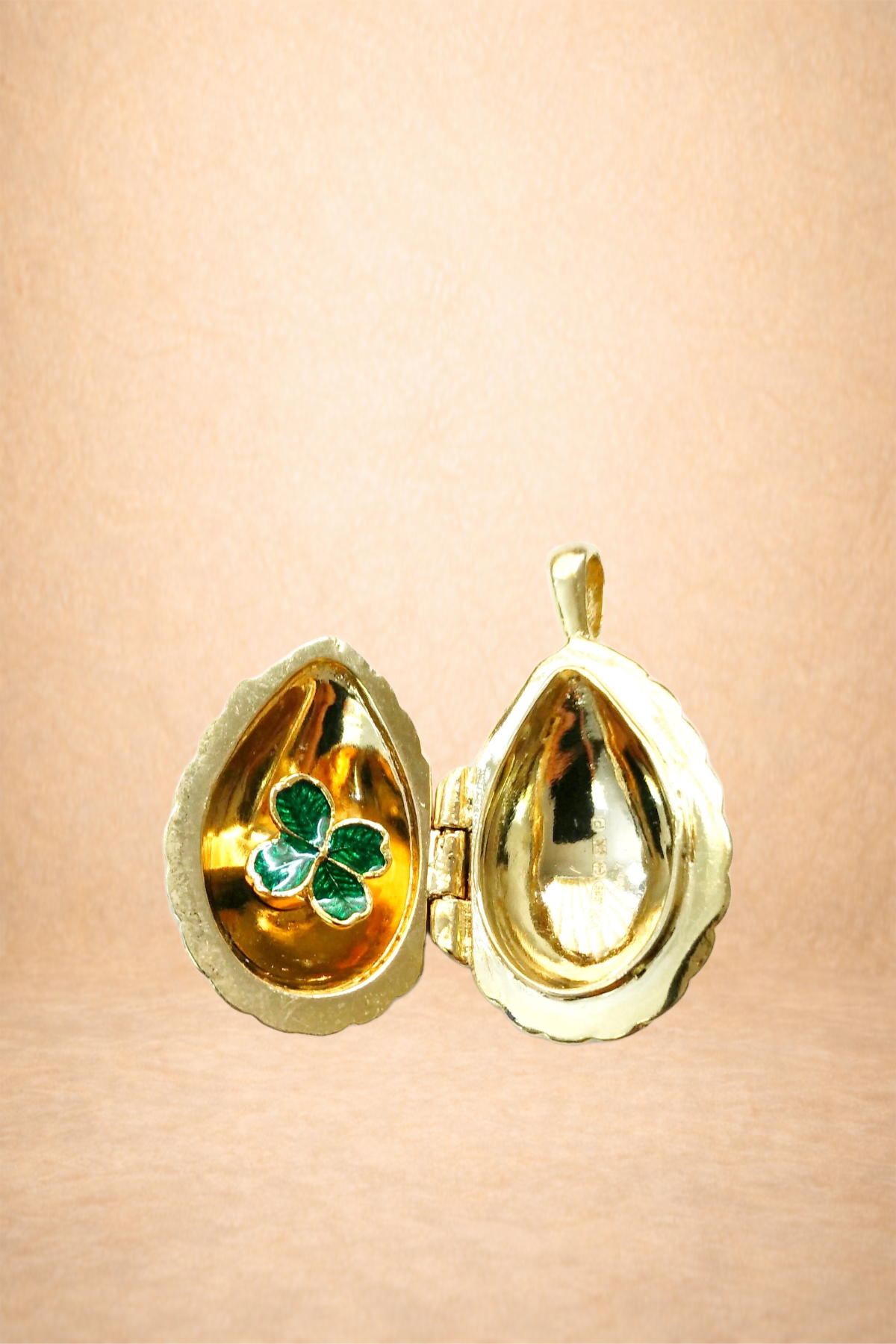 A gold jewelry box in the shape of a seashell, with a four-leaf clover design inside, against a soft pink background.