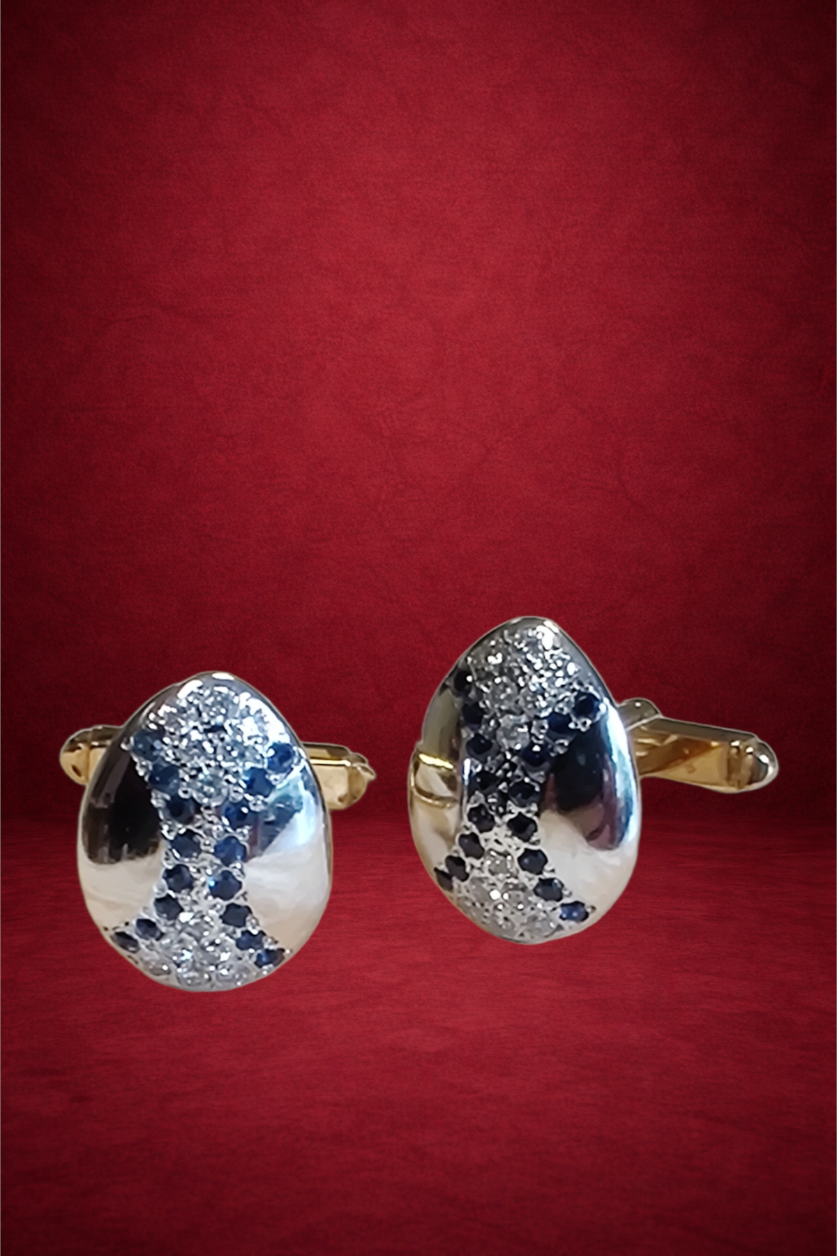 Pair of gold and silver earrings with teardrop shape, decorated with small diamonds and black stones, placed on a red background.
