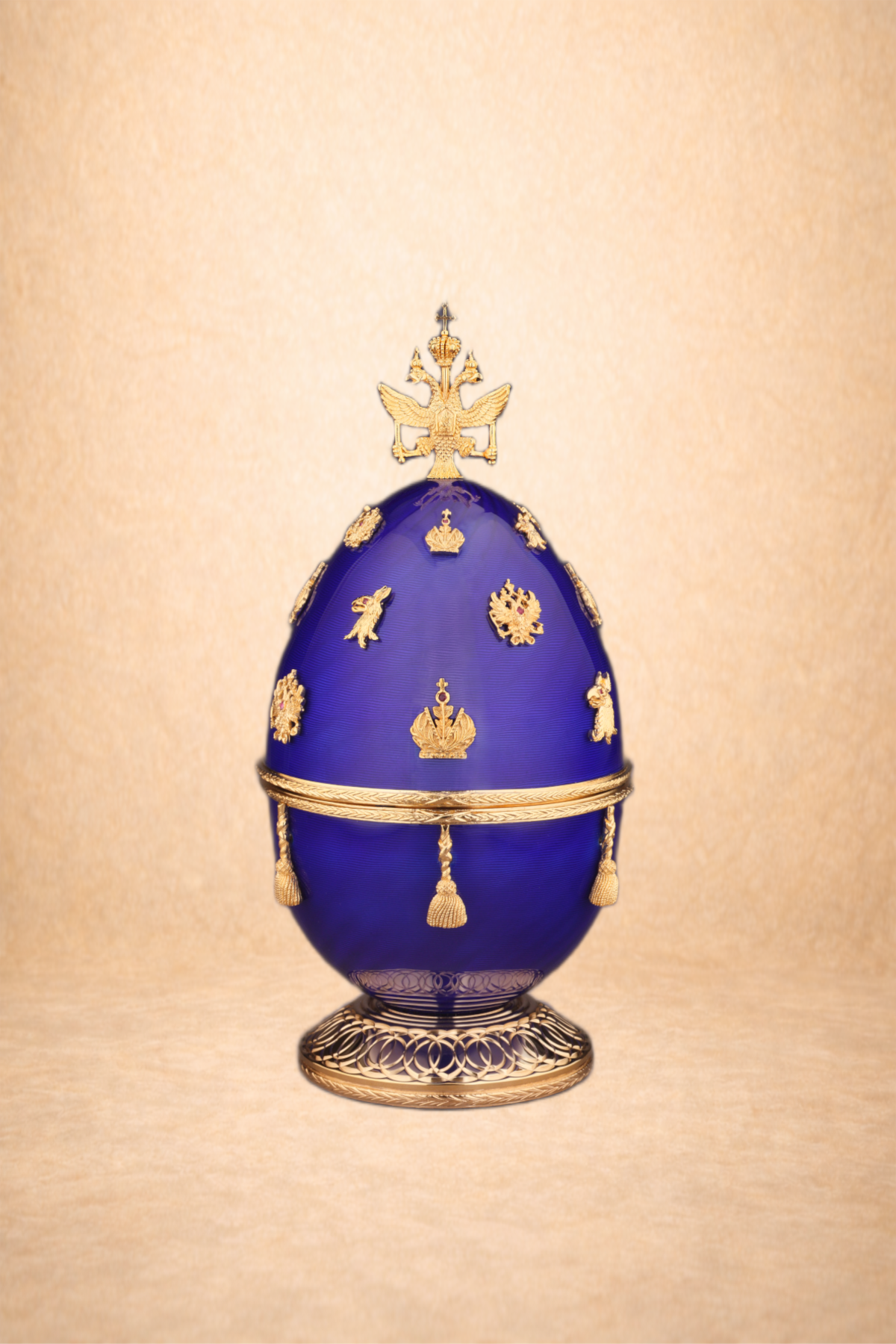 A decorative blue and gold ceremonial egg with intricate gold embellishments and a crown on top, set against a beige background.
