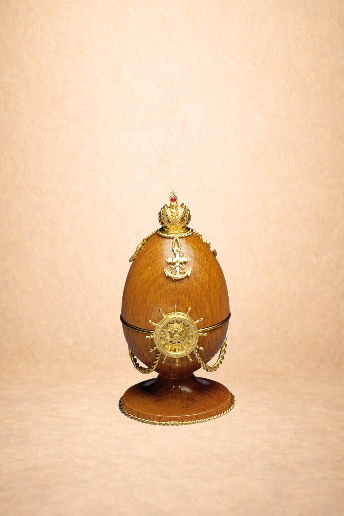 Decorative wooden egg with gold nautical-themed ornaments, including an anchor, ship wheel, and crown, displayed on a wooden stand.