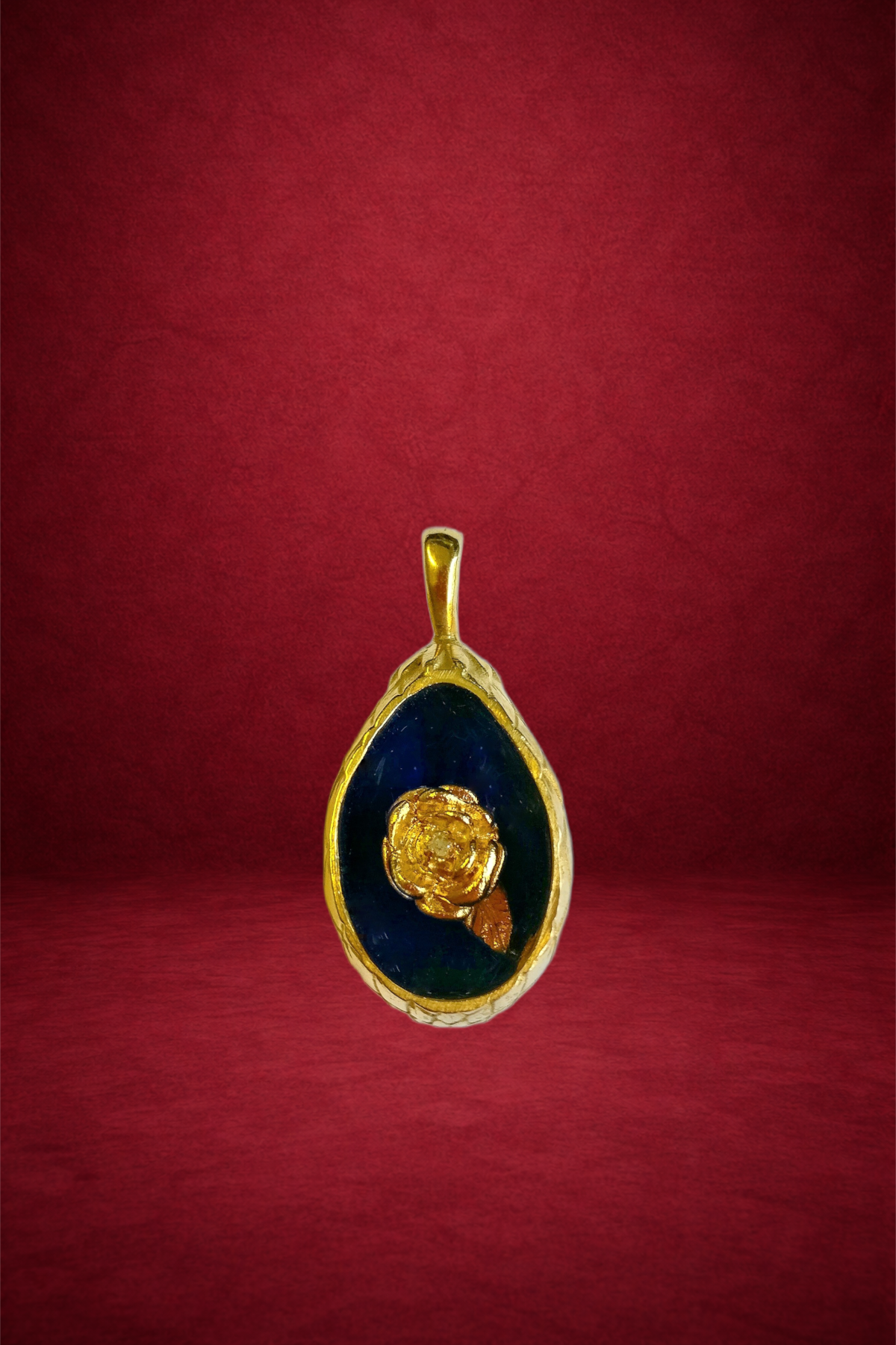 Gold pendant with a dark blue background and a yellow rose design in the center, hanging against a red backdrop.