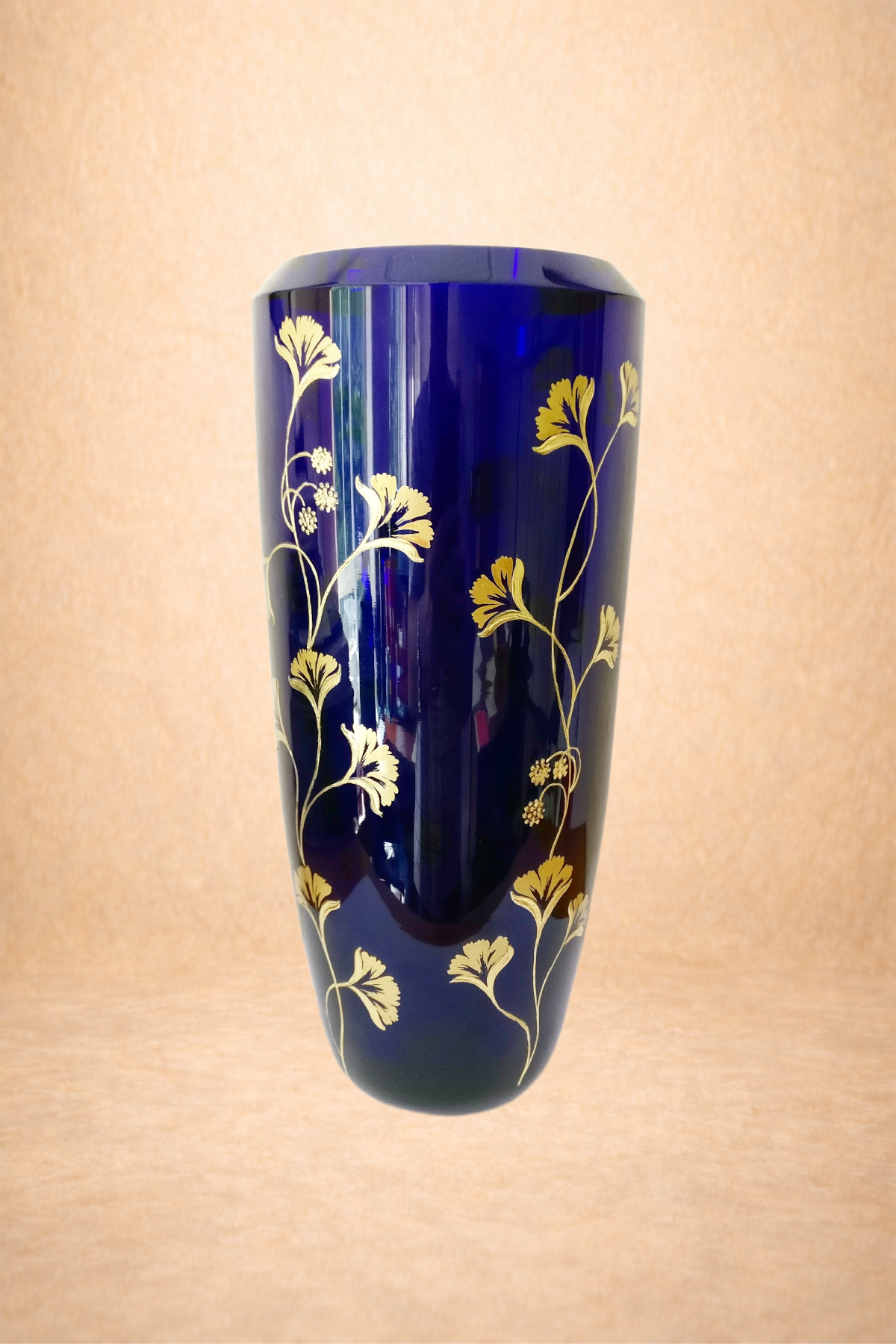 A dark blue vase with gold floral patterns displayed against a beige background.