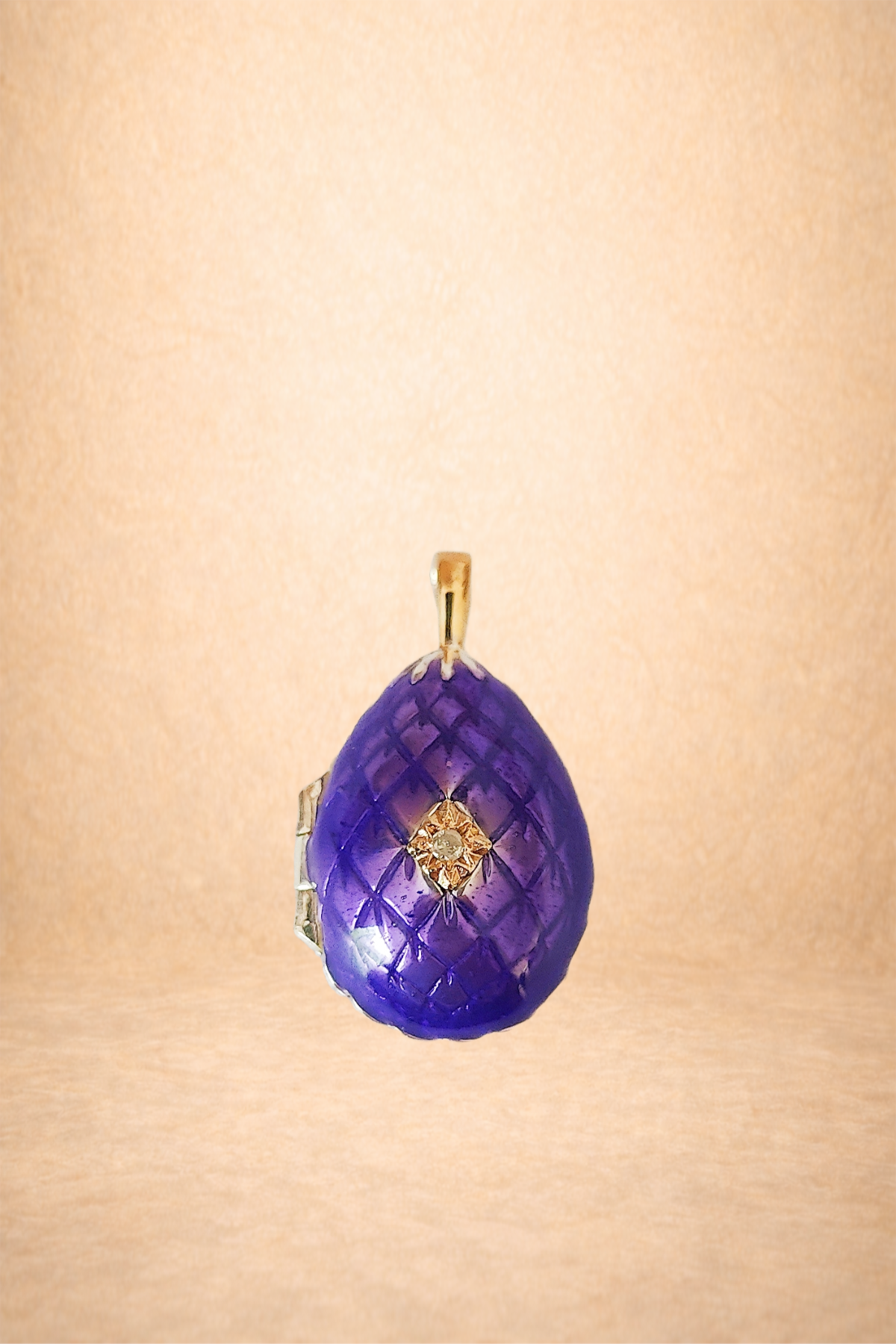 A purple, quilted glass pendant with a gold bail, featuring a small central gemstone and decorative gold accents.