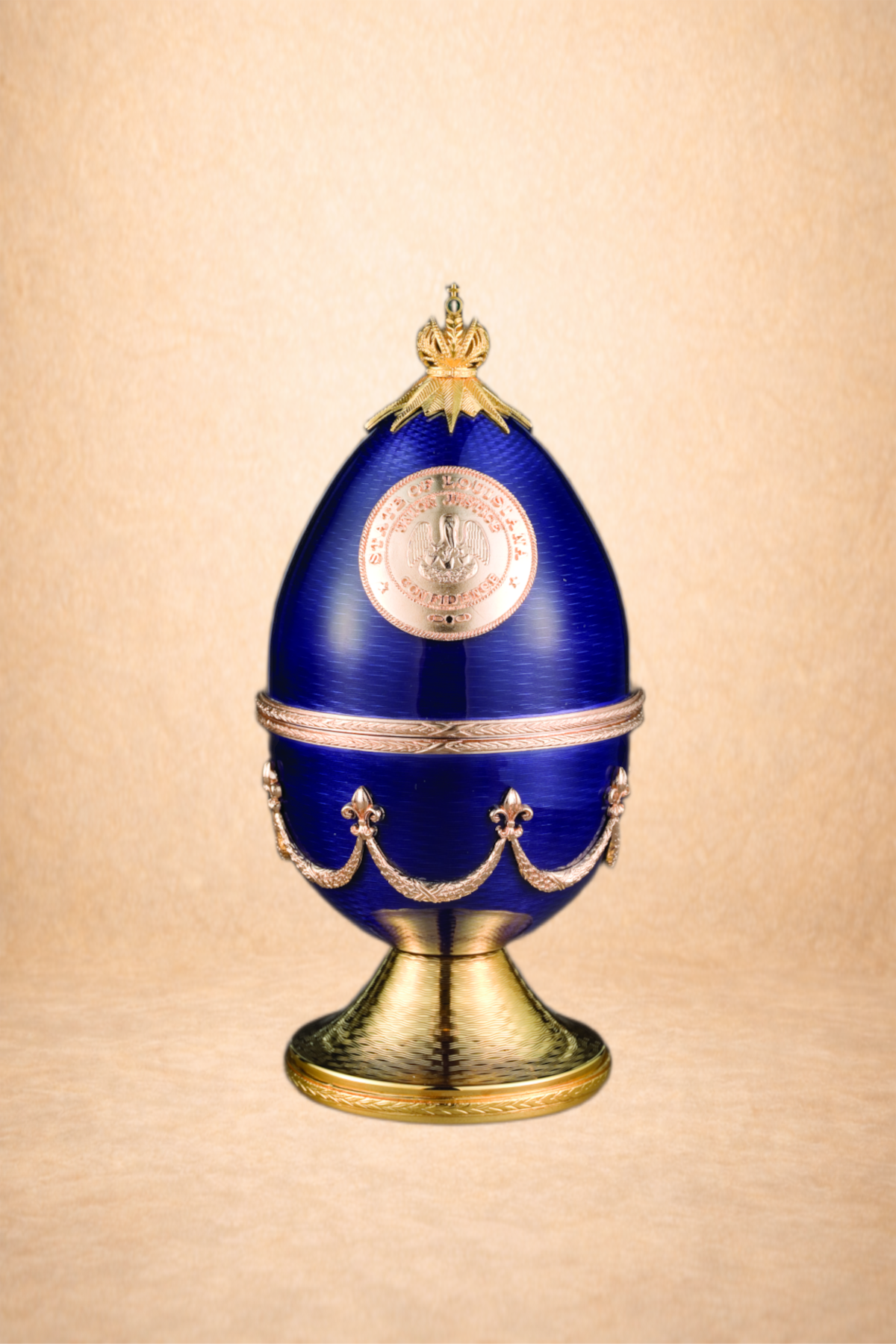 A blue and gold decorative egg with a crest and metallic embellishments on a gold stand.