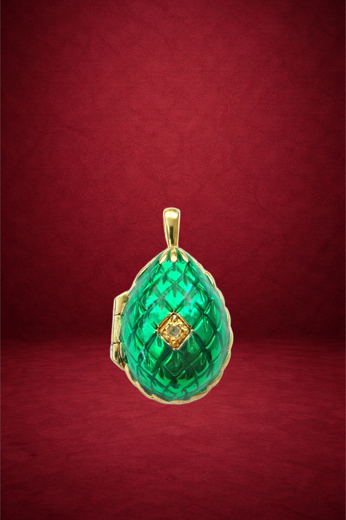 A gold pendant with a green, textured, cathedral-shaped gemstone and a small diamond at its center, set against a red background.