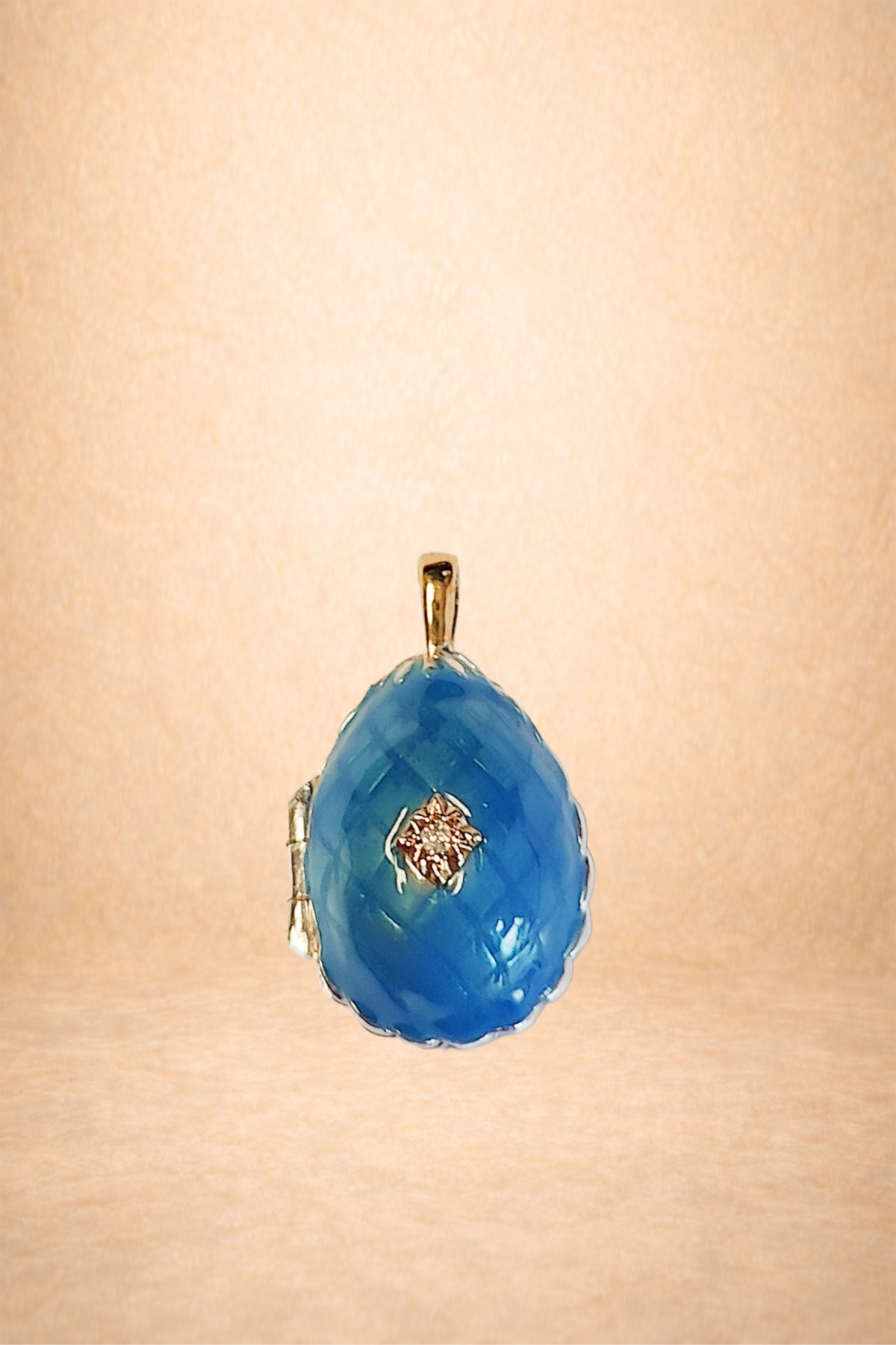 A blue gemstone pendant with a small diamond at the center, hanging from a gold bail on a light orange background.