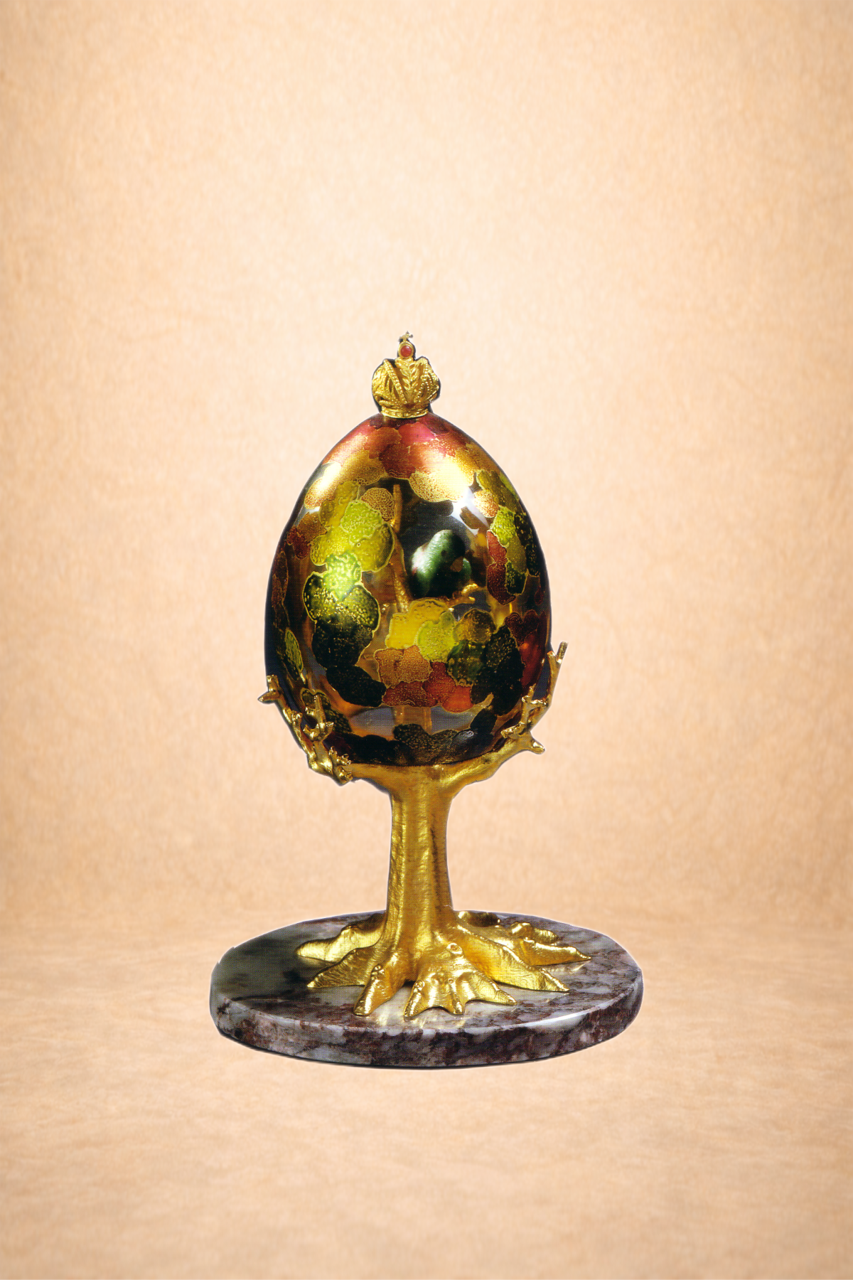 A decorative art piece featuring an egg-shaped object with colorful pattern, topped with a small crown, mounted on a golden duck-like stand with webbed feet, on a round marble base.