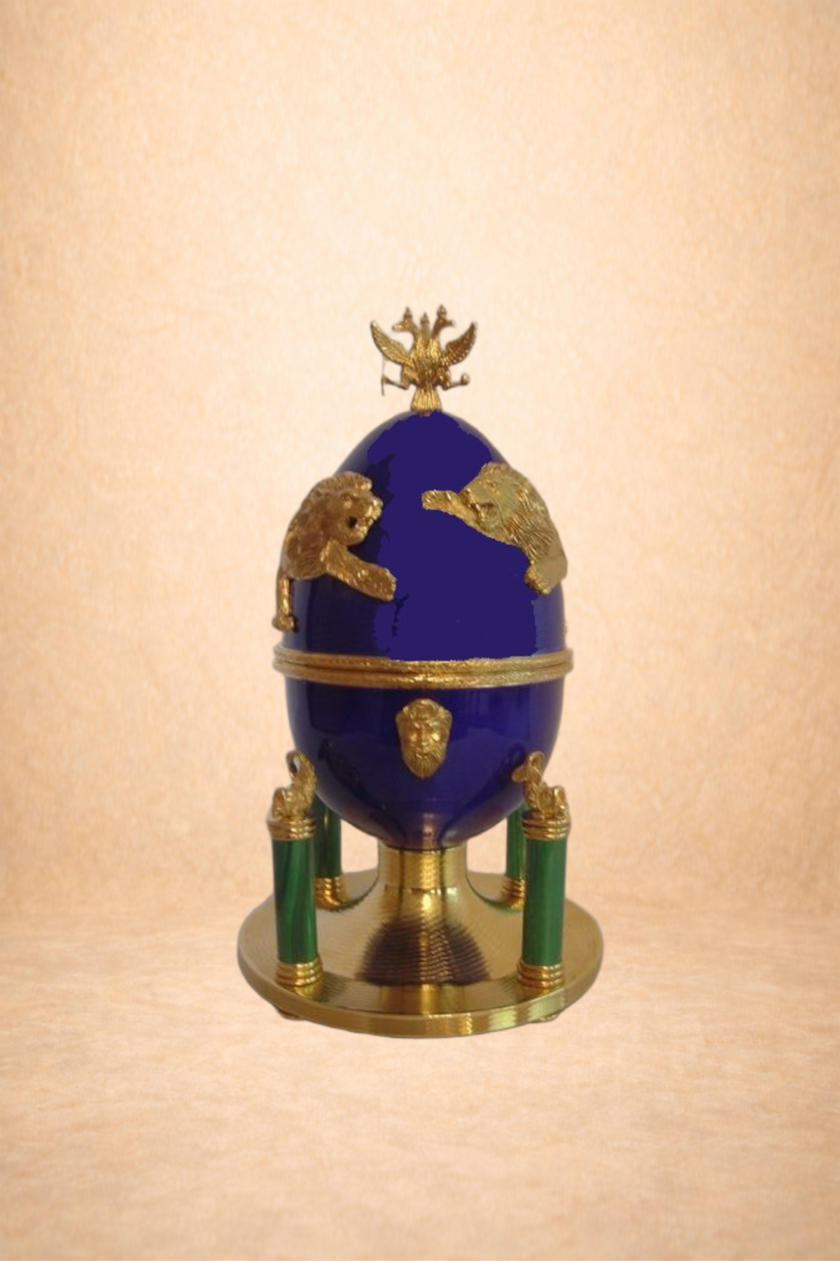 A decorative, ornate blue and gold egg-shaped object with gold animal figures and a golden double-headed eagle on top, supported by green and gold legs, set against a plain beige background.
