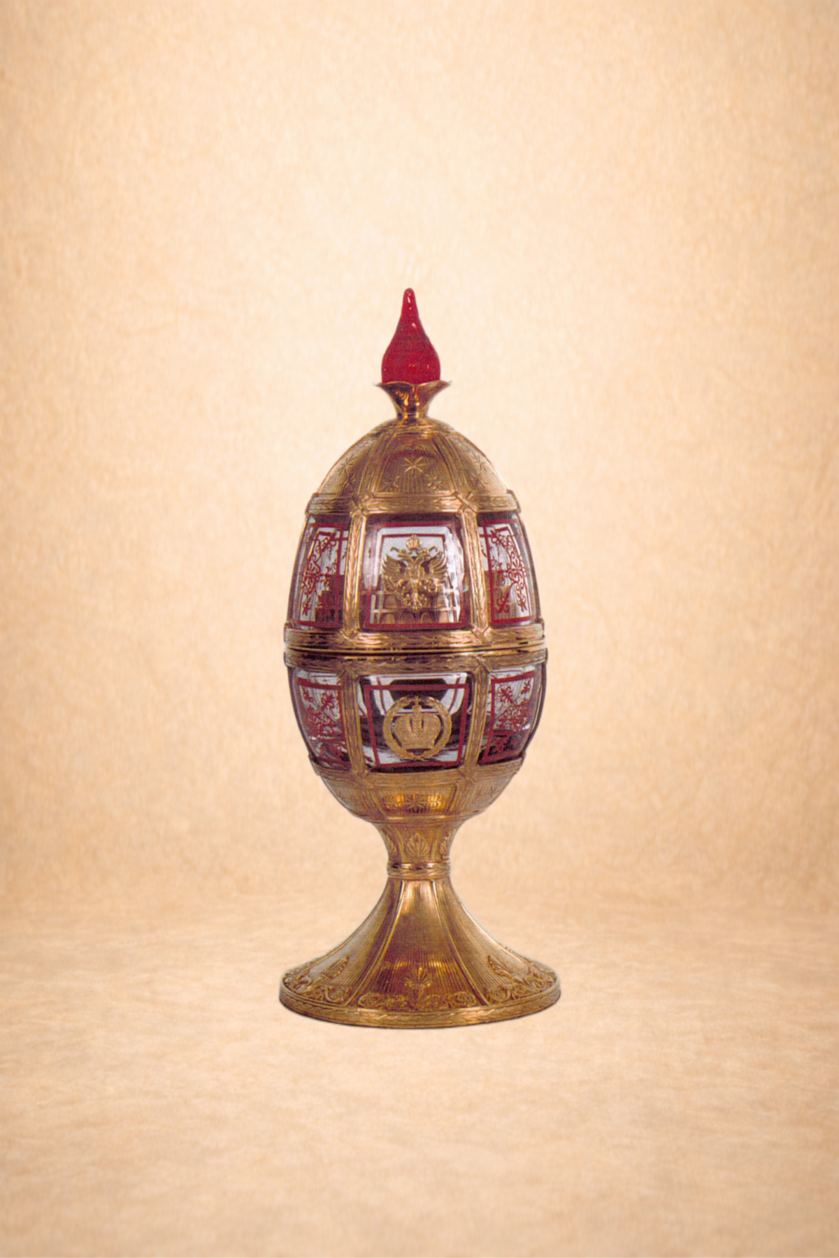 An ornate chalice with a gold base and a glass upper section, topped with a red finial.