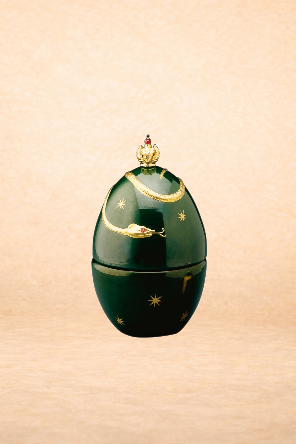 A decorative container with a dark green, egg-shaped exterior, adorned with gold stars and a gold chain depicted as a snake. It is topped with a gold crown that has a red gem, resembling a royal or imperial insignia.