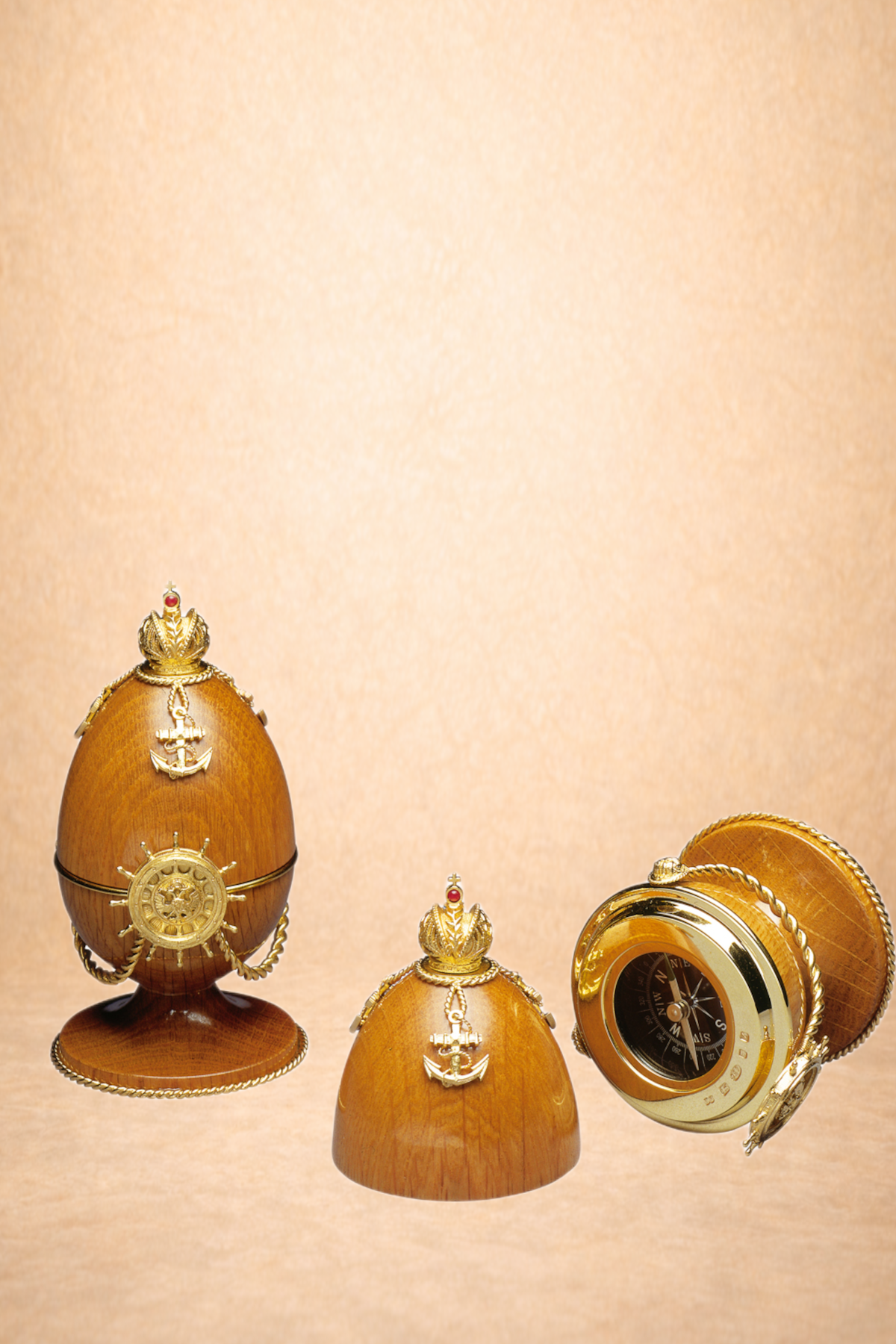 Decorative wooden eggs with gold naval-themed embellishments, and a compass, set against a plain beige background.