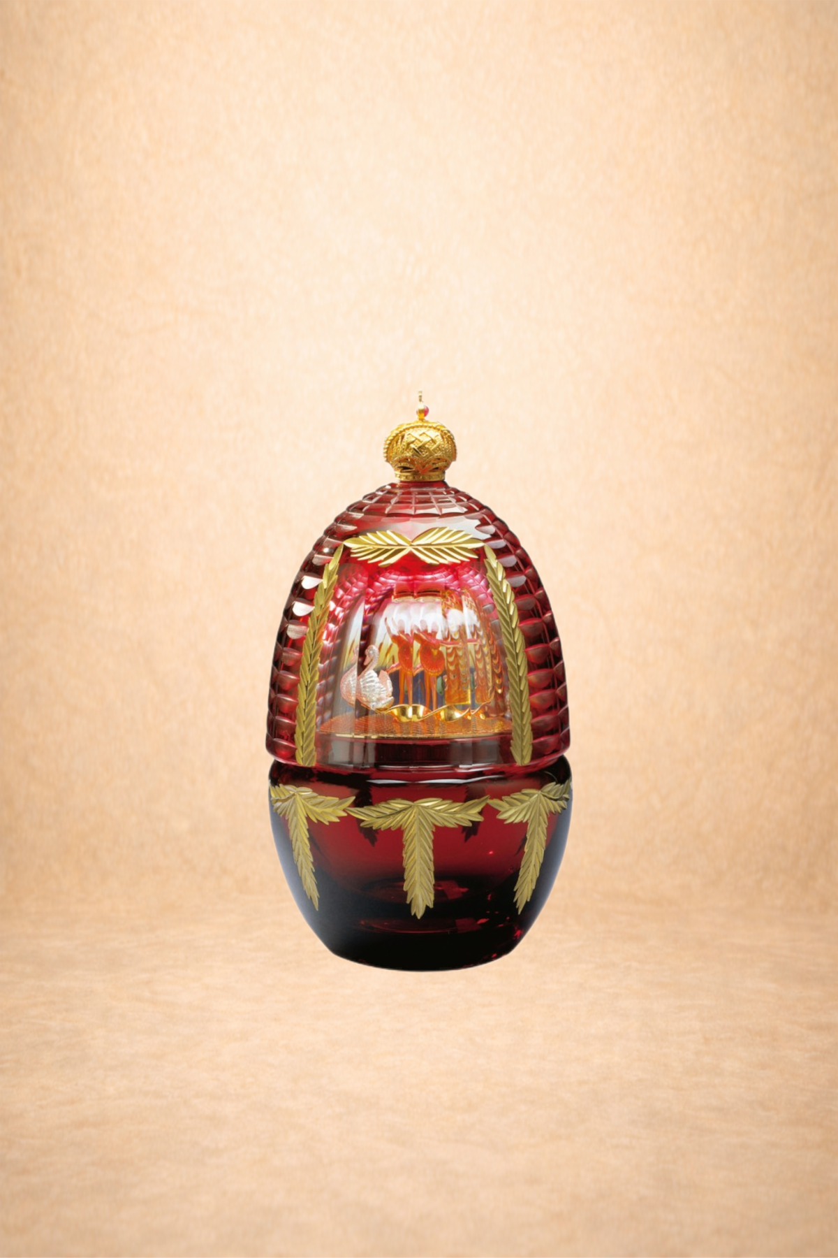 A decorative glass ornament with gold accents, shaped like an egg with a domed top, featuring a hinged lid. Inside the glass, there is a miniature scene with figures and ornate decorations. The background is a plain, light-colored surface.
