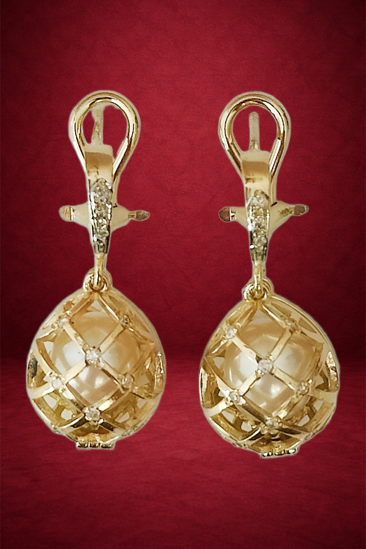 Gold earrings with intricate lattice design and small embedded gemstones on a red background.