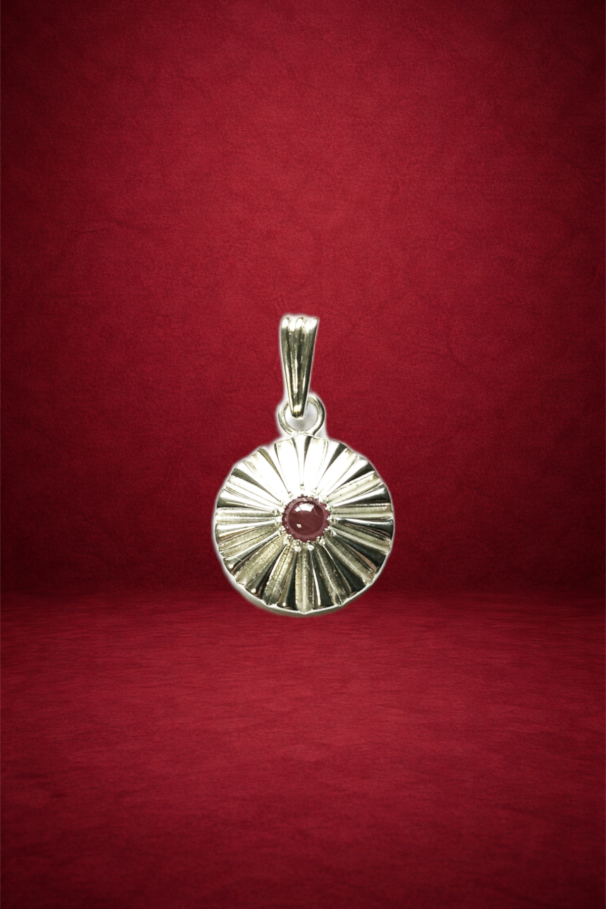 Silver pendant with a circular design and a red gemstone in the center, hanging against a red background.