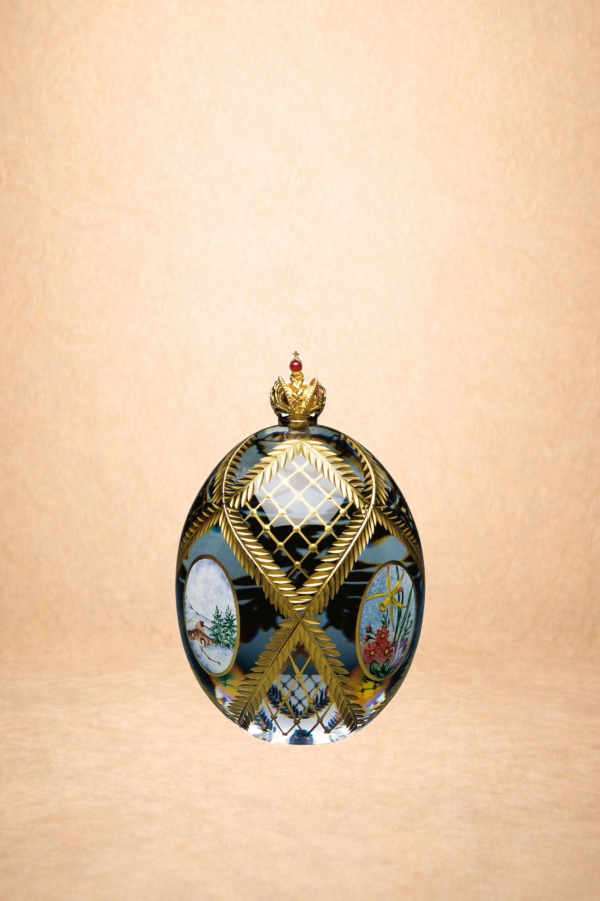 Decorative glass egg with floral and nature paintings, gold leaf designs, and a small gold crown with a red gem on top against a beige background.