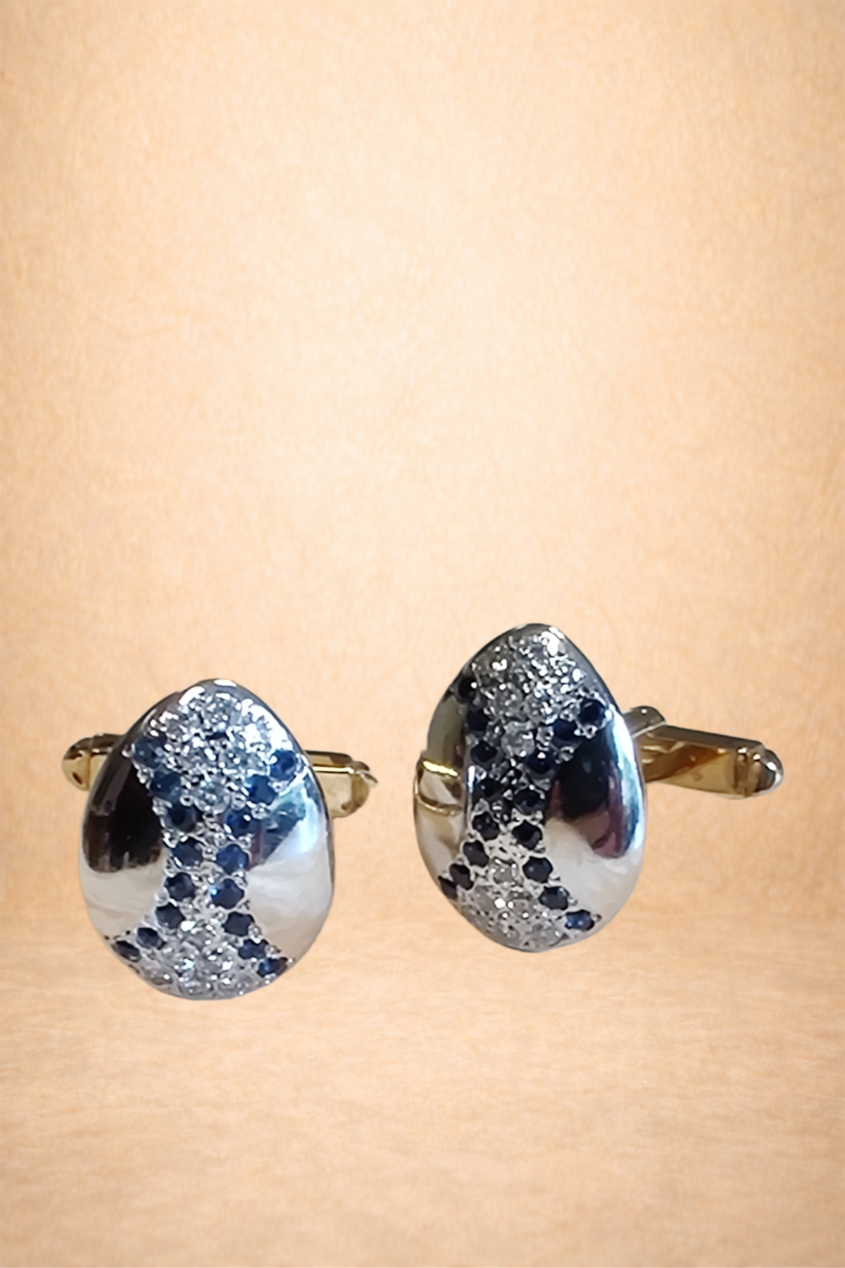 Pair of silver and black teardrop-shaped earrings with embedded sparkling crystals on a beige background.