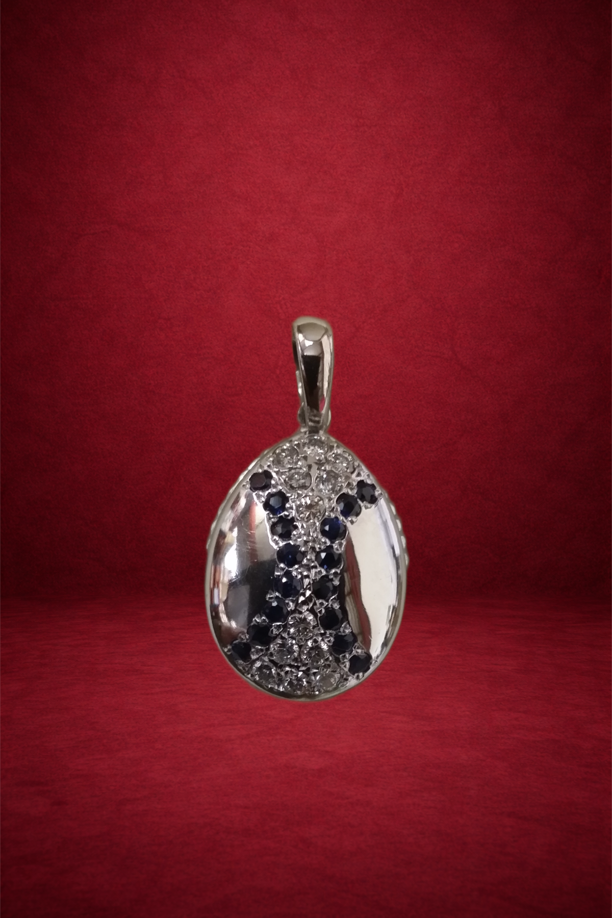 Silver pendant with a peace symbol design, encrusted with black and clear gemstones, hanging against a red background.