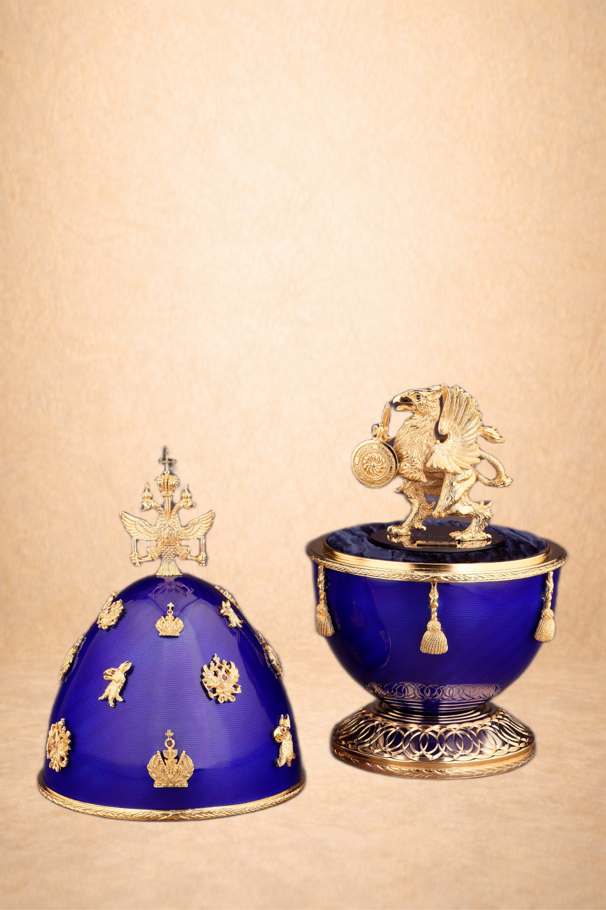Two ornate blue and gold ceremonial objects: one shaped like a crown with gold embellishments and a double-headed eagle crest on top; the other is a blue bowl with gold accents and a gold lion figurine holding a coin on top.