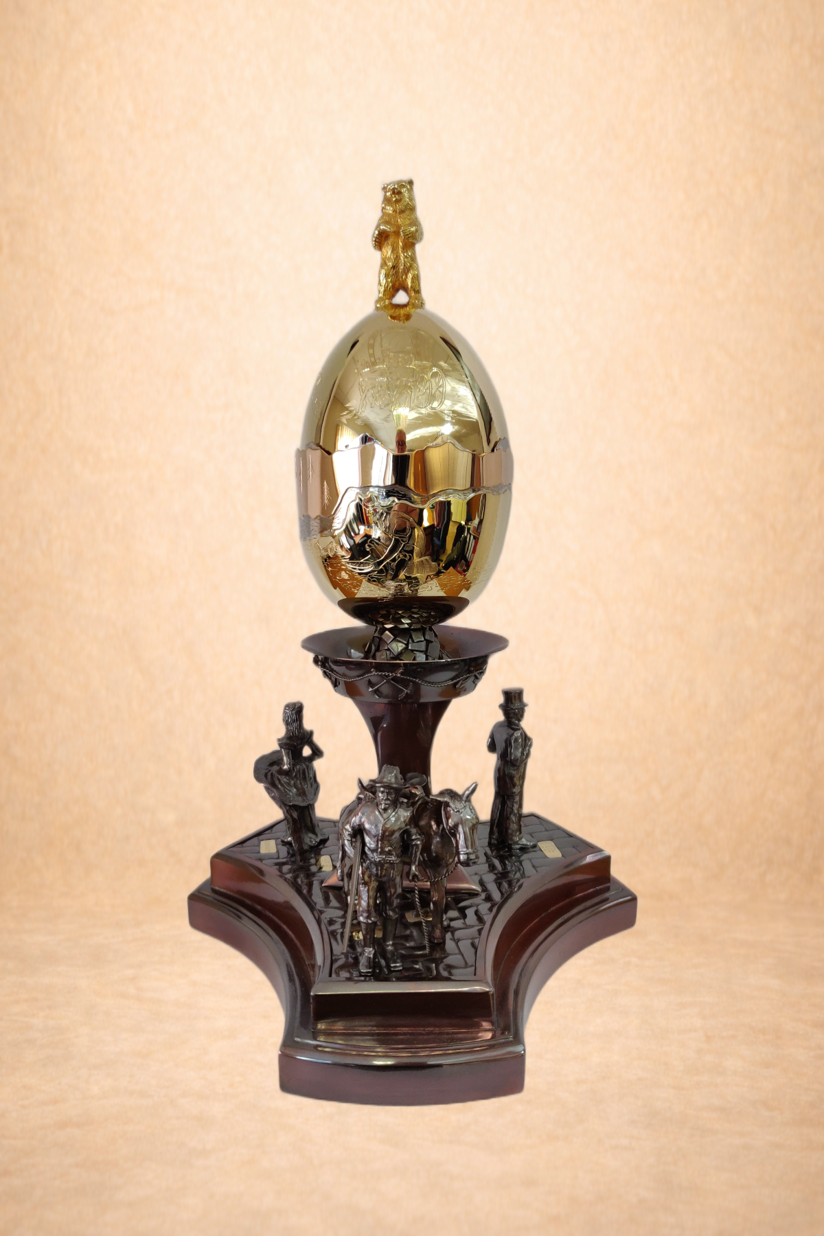 A trophy with a gold egg at the top, featuring a small bear figurine on it. The trophy has a base with metallic figurines of cowboys and horses, and the overall structure is made of dark wood and metal.