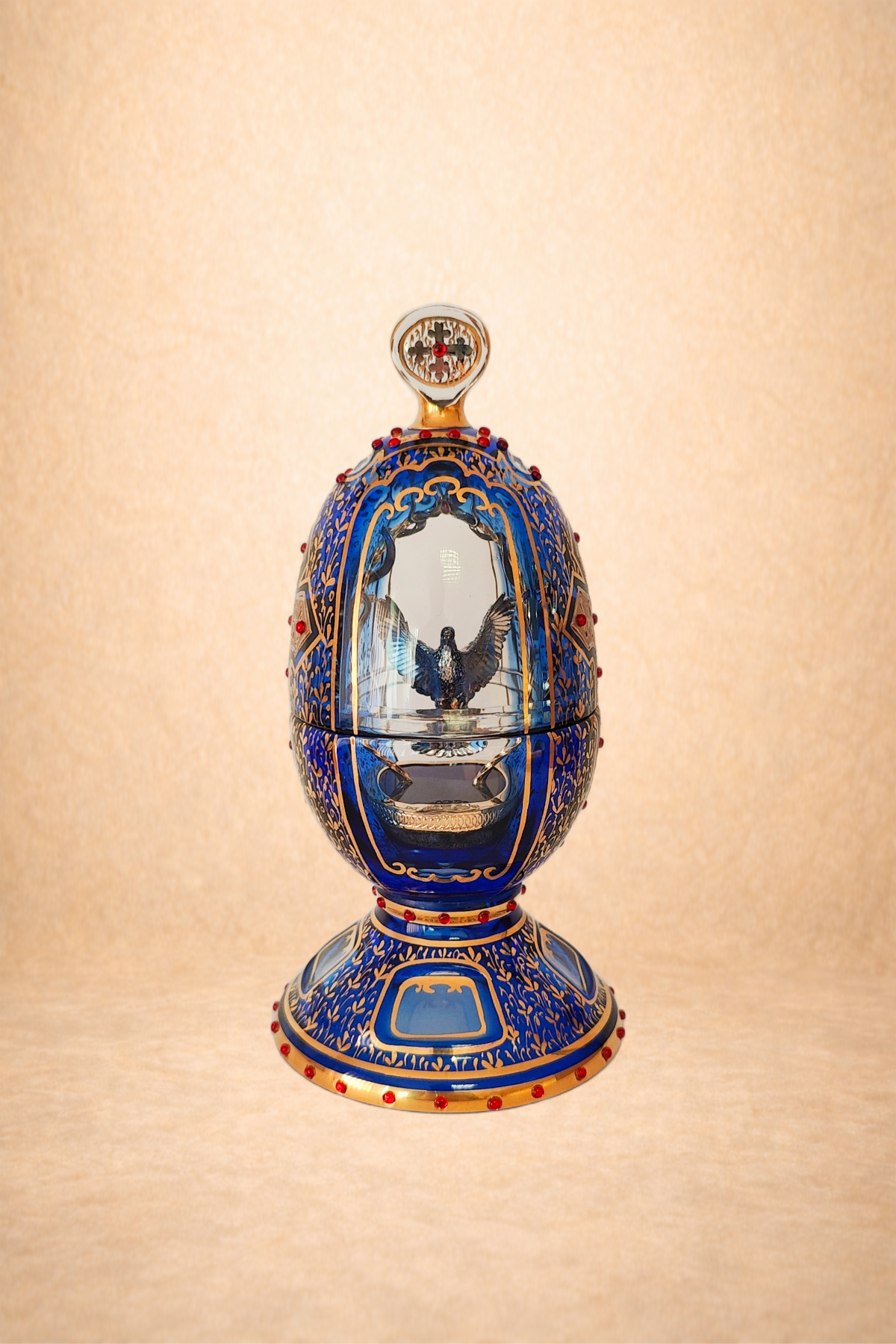 An ornate, decorative egg-shaped object with blue and gold patterns, containing a bird figure inside, and a small mirror at the top.