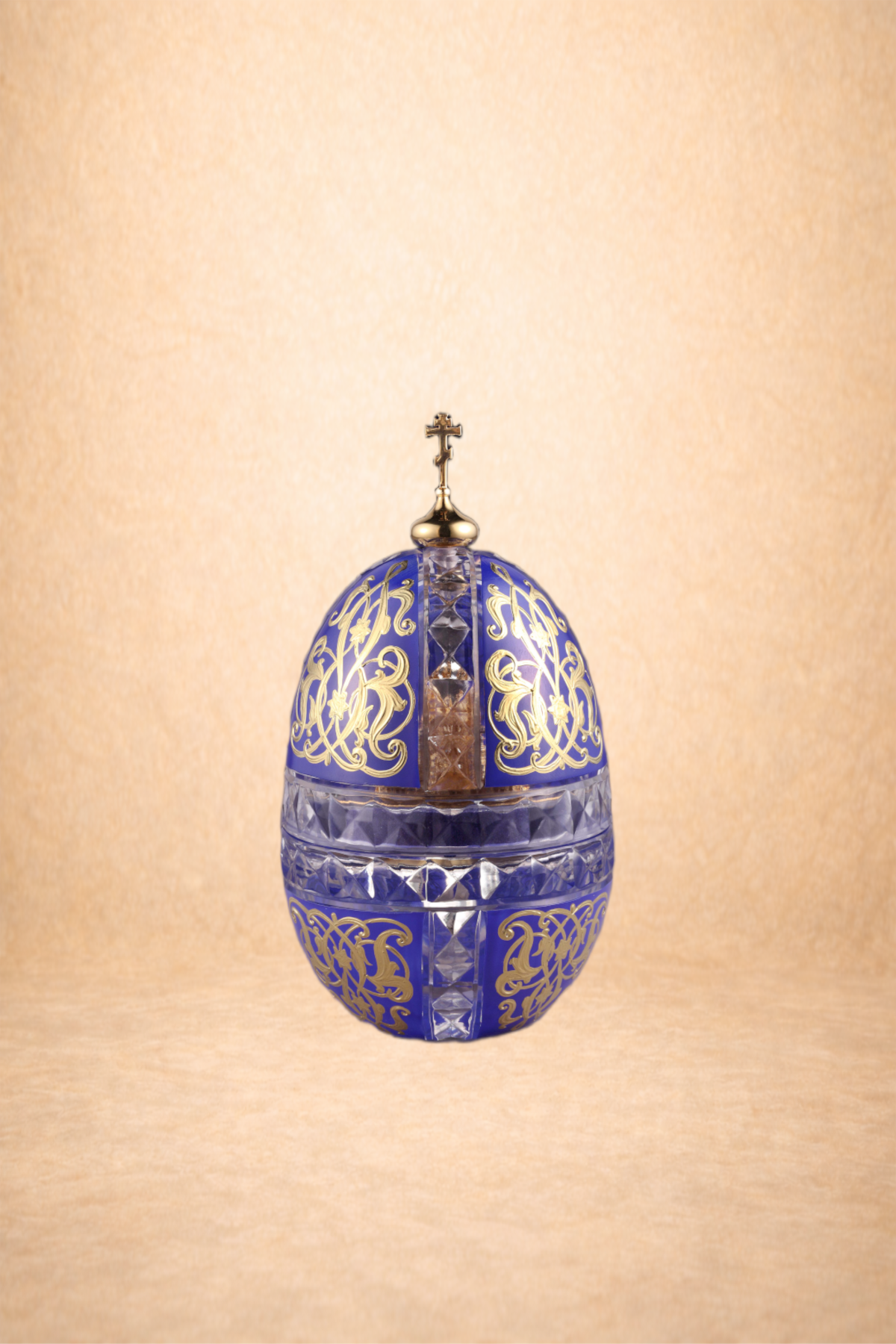 A decorative glass Easter egg with blue and gold designs, topped with a small cross.
