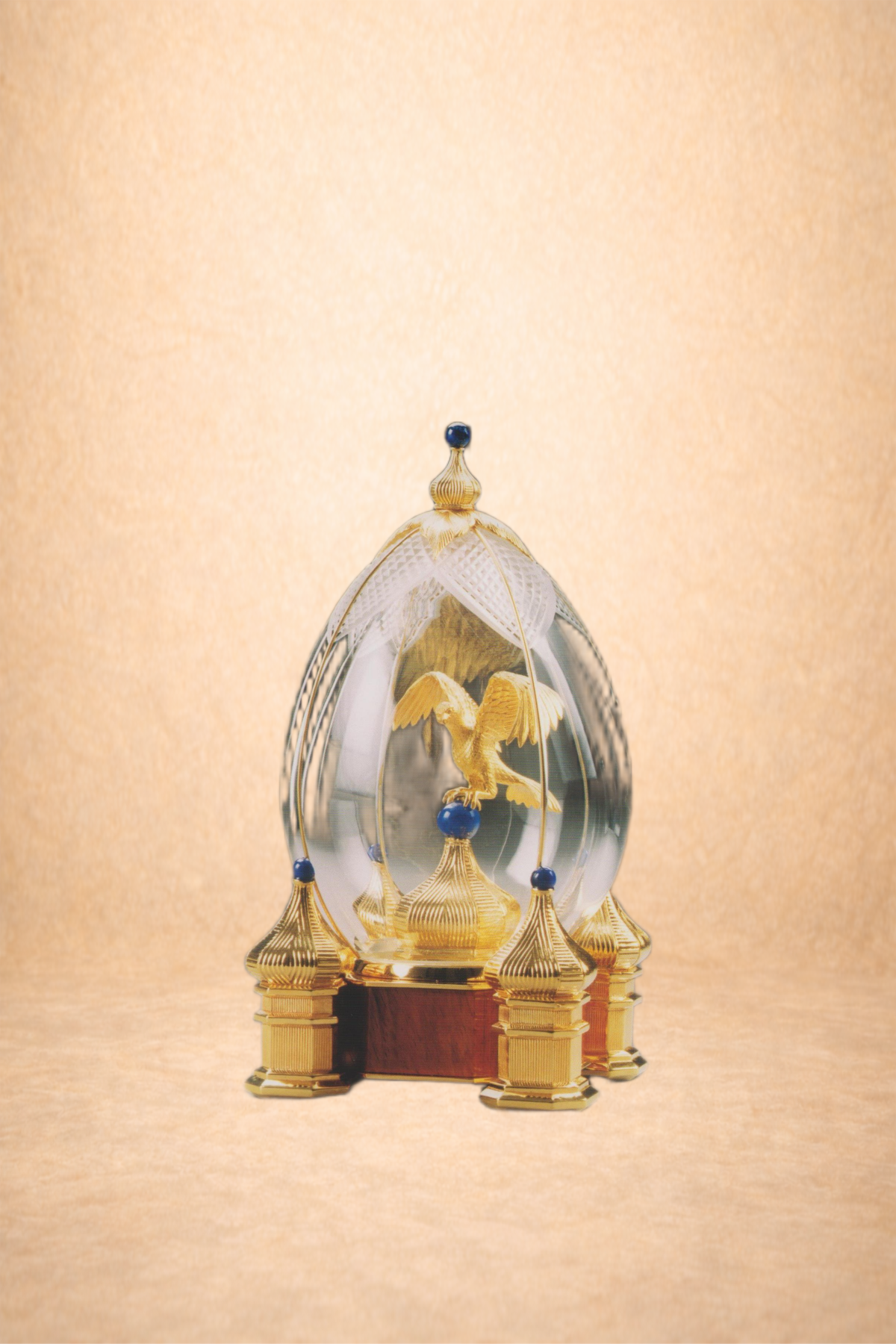 A decorative glass dome with a gold eagle inside, mounted on a wooden base with gold accents, set against a golden background.