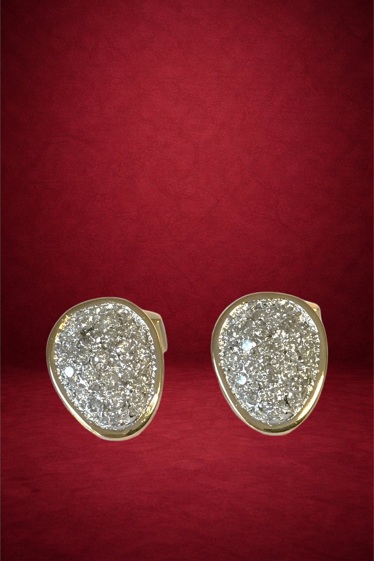 Pair of gold earrings with diamond-encrusted oval-shaped tops on a red surface.