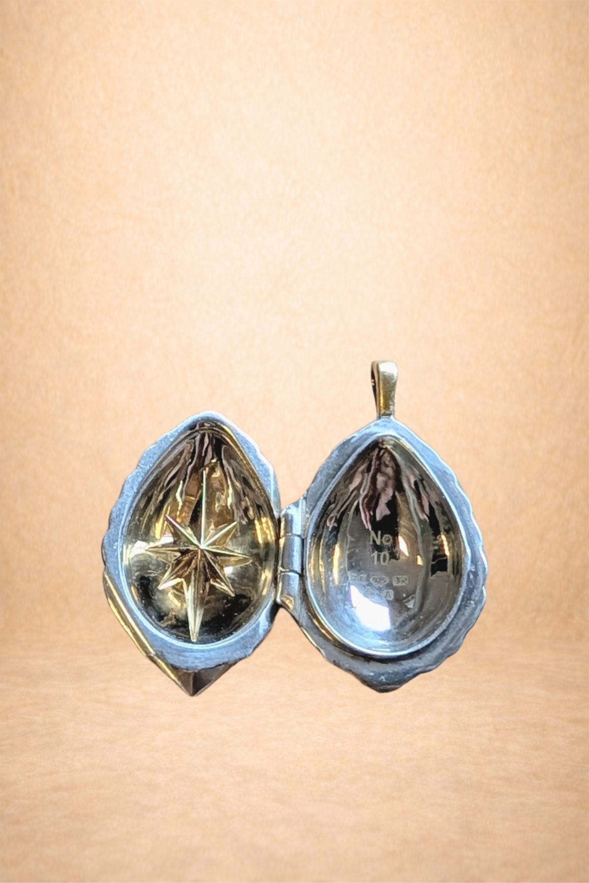 A small silver locket with a heart-shaped cover, open to reveal a gold star inside on a light brown background.