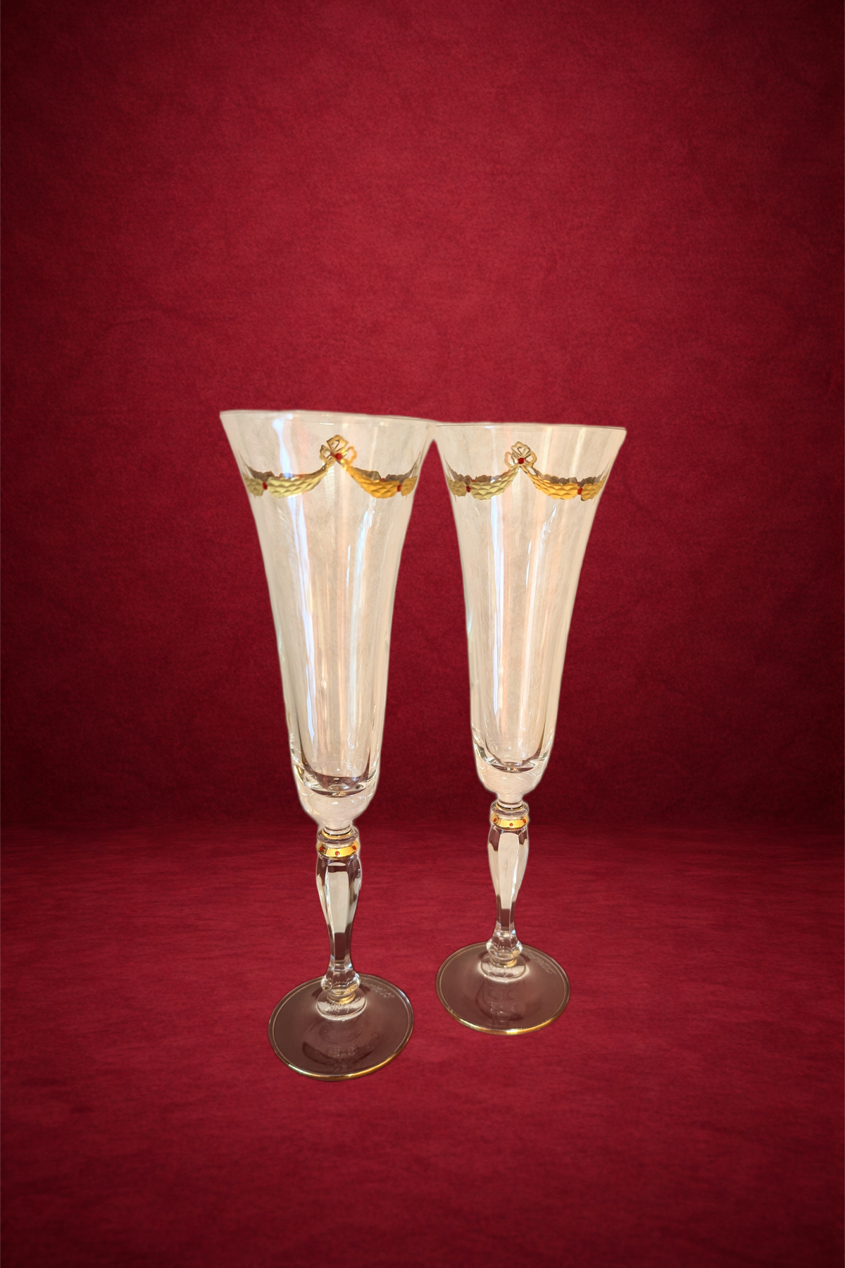 Two elegant champagne flutes with gold and red decorative bands near the top, set against a red textured background.