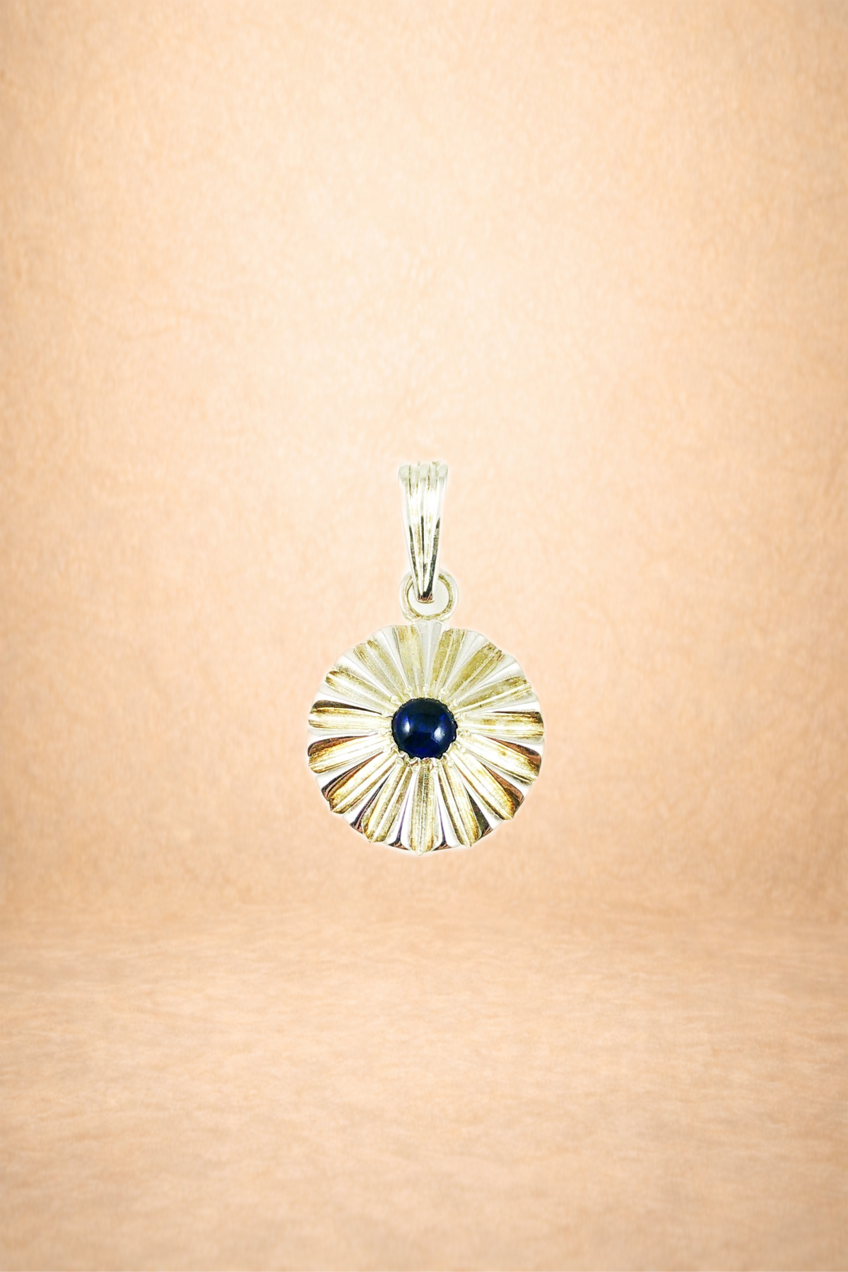 Silver pendant with a black gemstone in center, shaped like a radiating sunburst, hanging on a chain against a tan background.