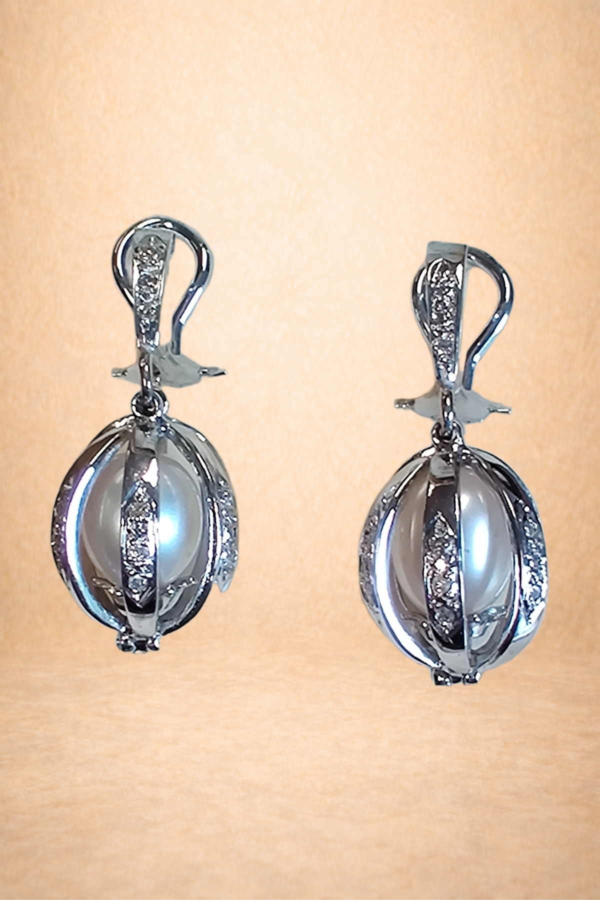 Elegant silver earrings with white pearls and embedded diamonds against a light orange background.