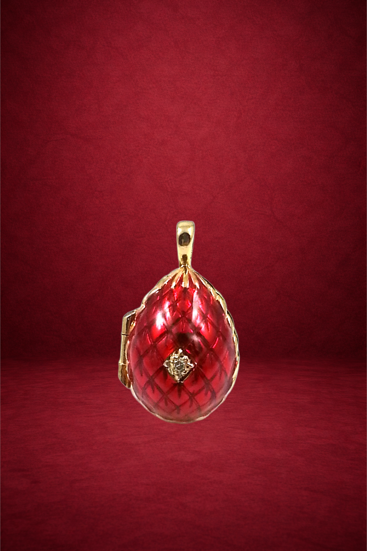 Red and gold teardrop pendant with intricate design and diamond accents, hanging against a red background.