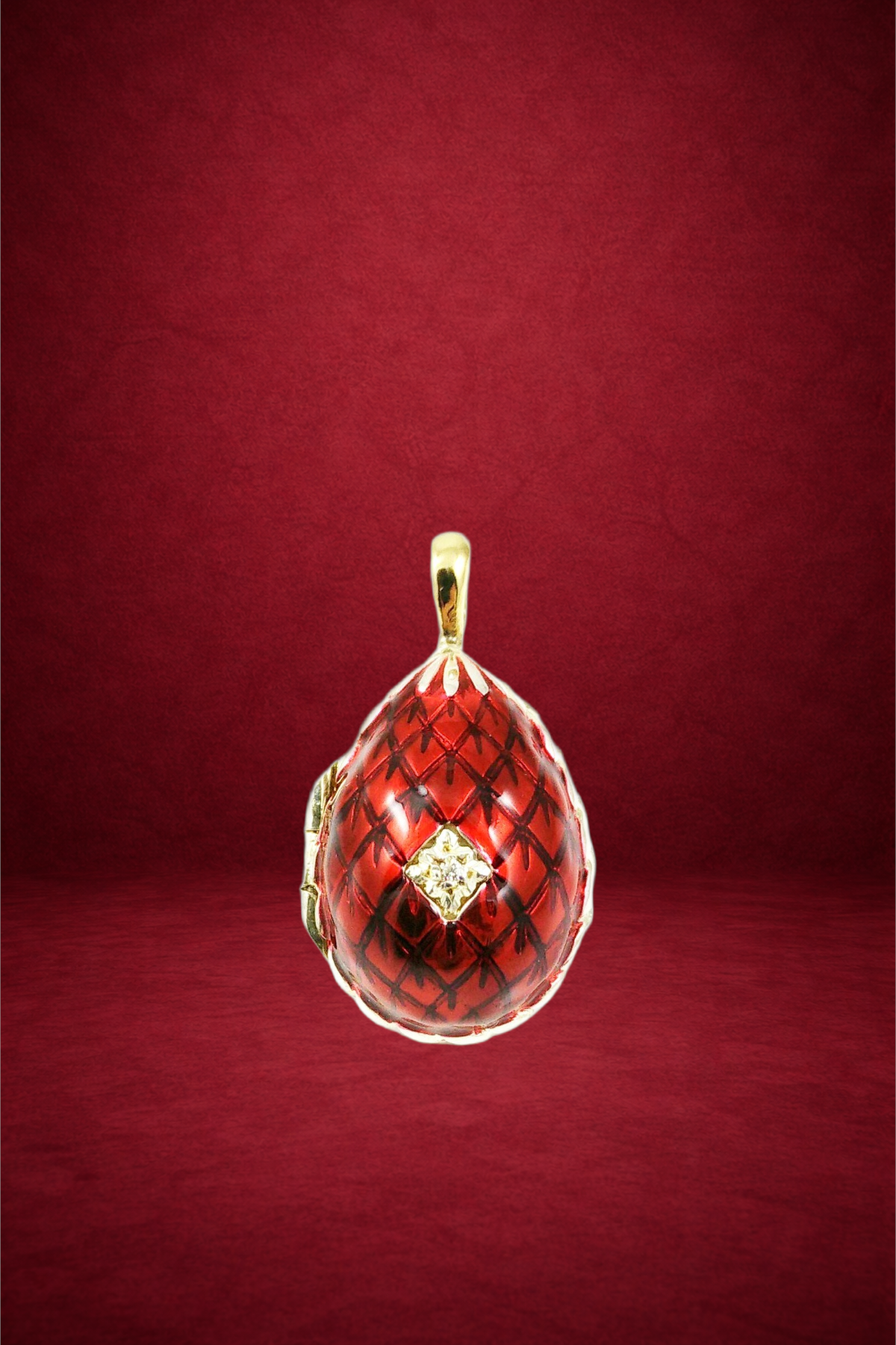 A gold pendant with a red, patterned, glass-like teardrop-shaped centerpiece, featuring a small diamond-like stone in the middle, against a solid red background.
