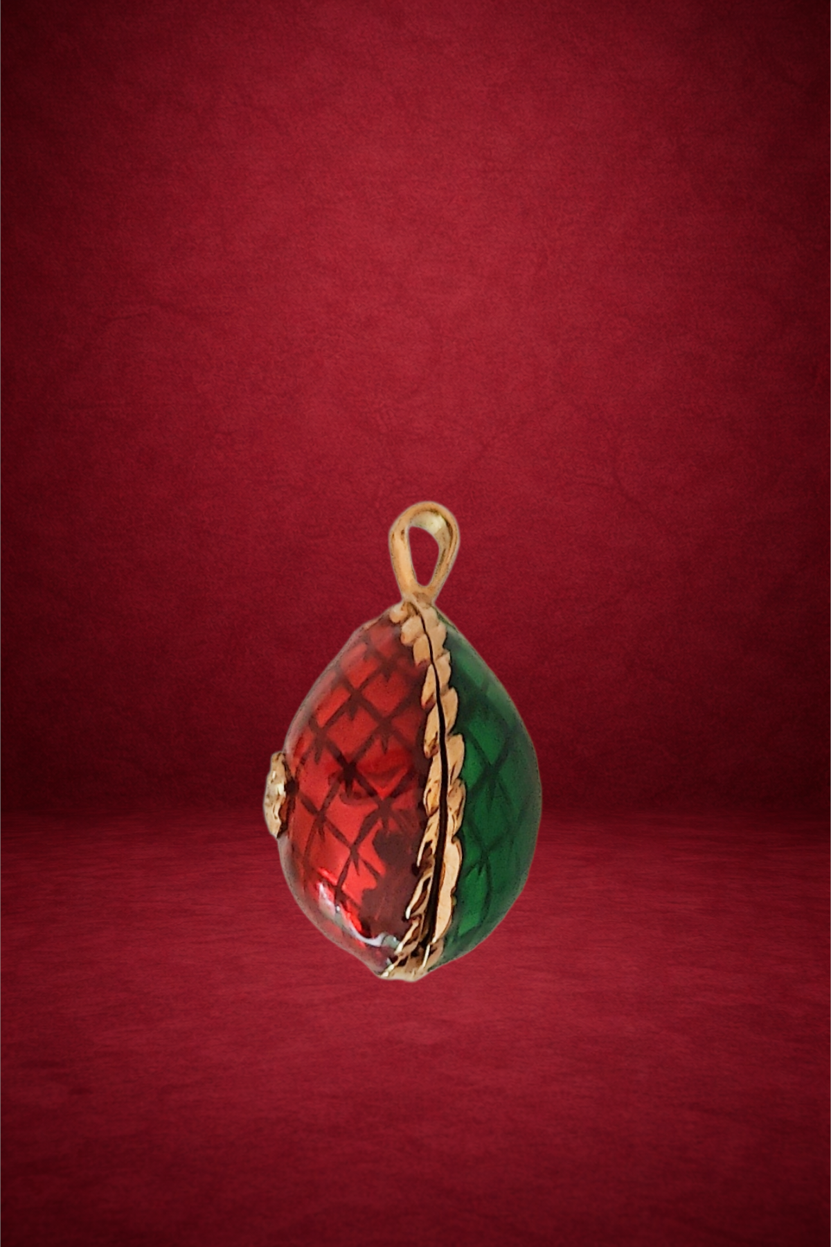 Glass ornament with red and green sections, gold edge, hanging loop on top, against a red background.