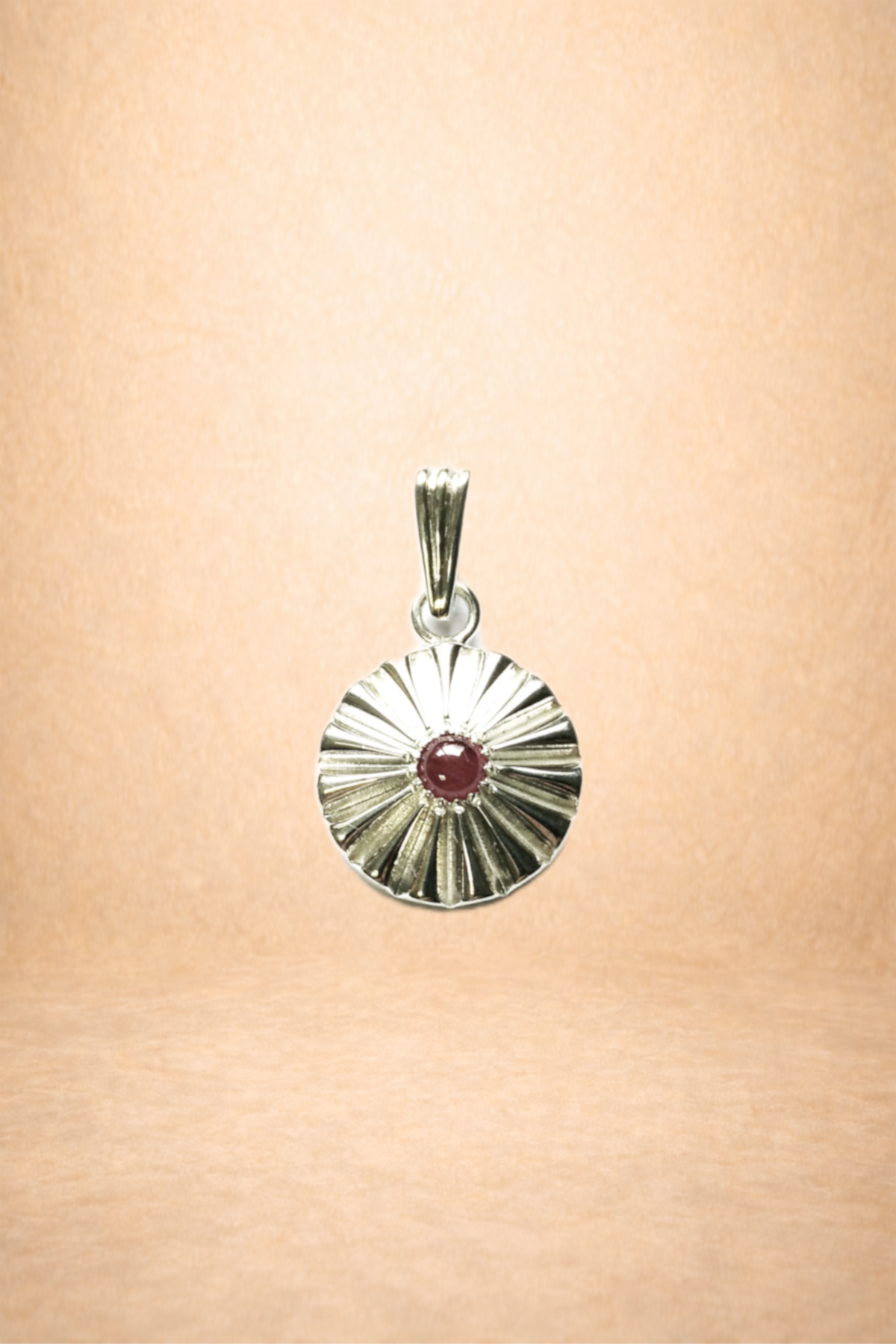 A silver pendant with a red gemstone in the center, hanging against a light-colored background.